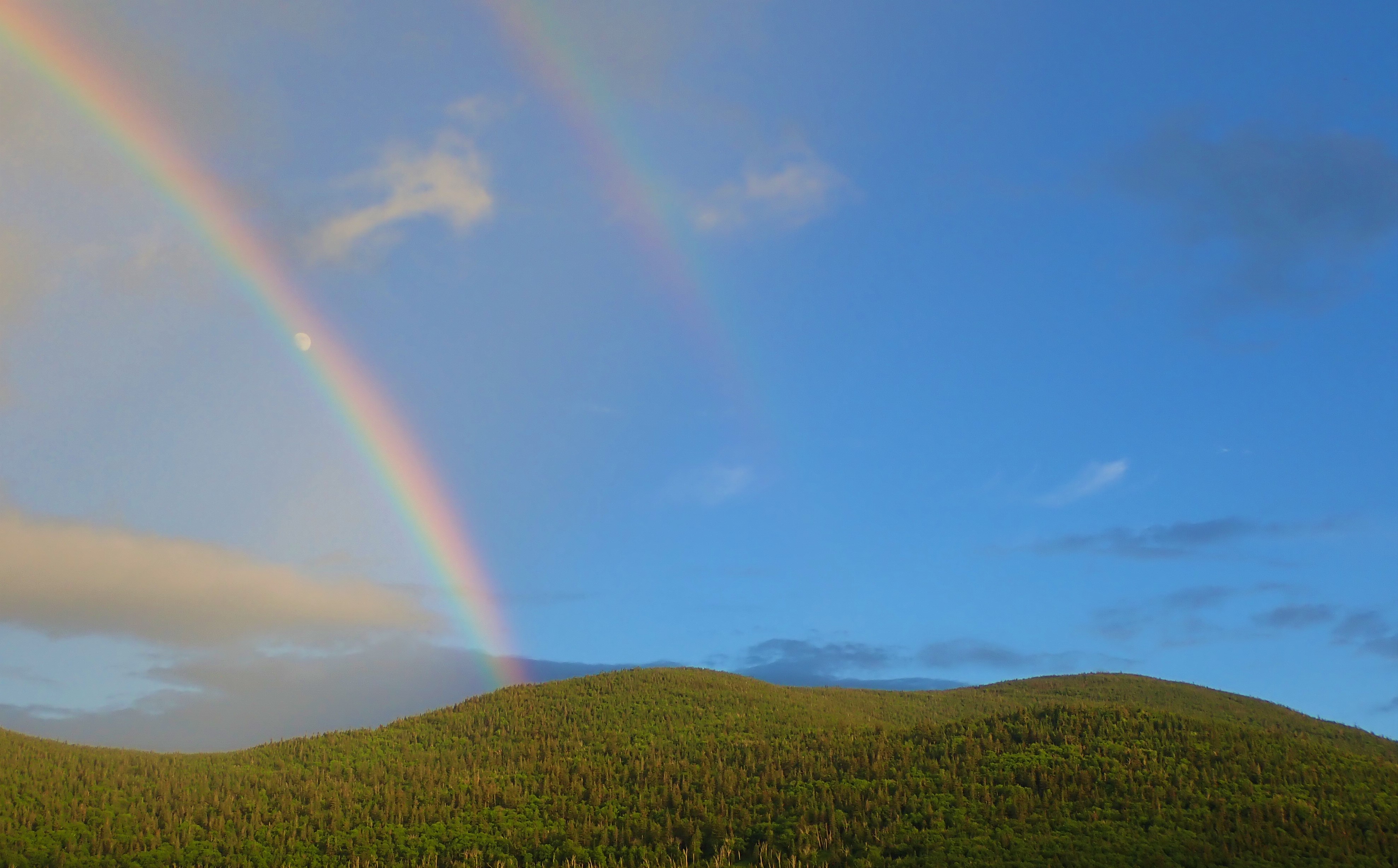 A rainbow arches over green mountains.