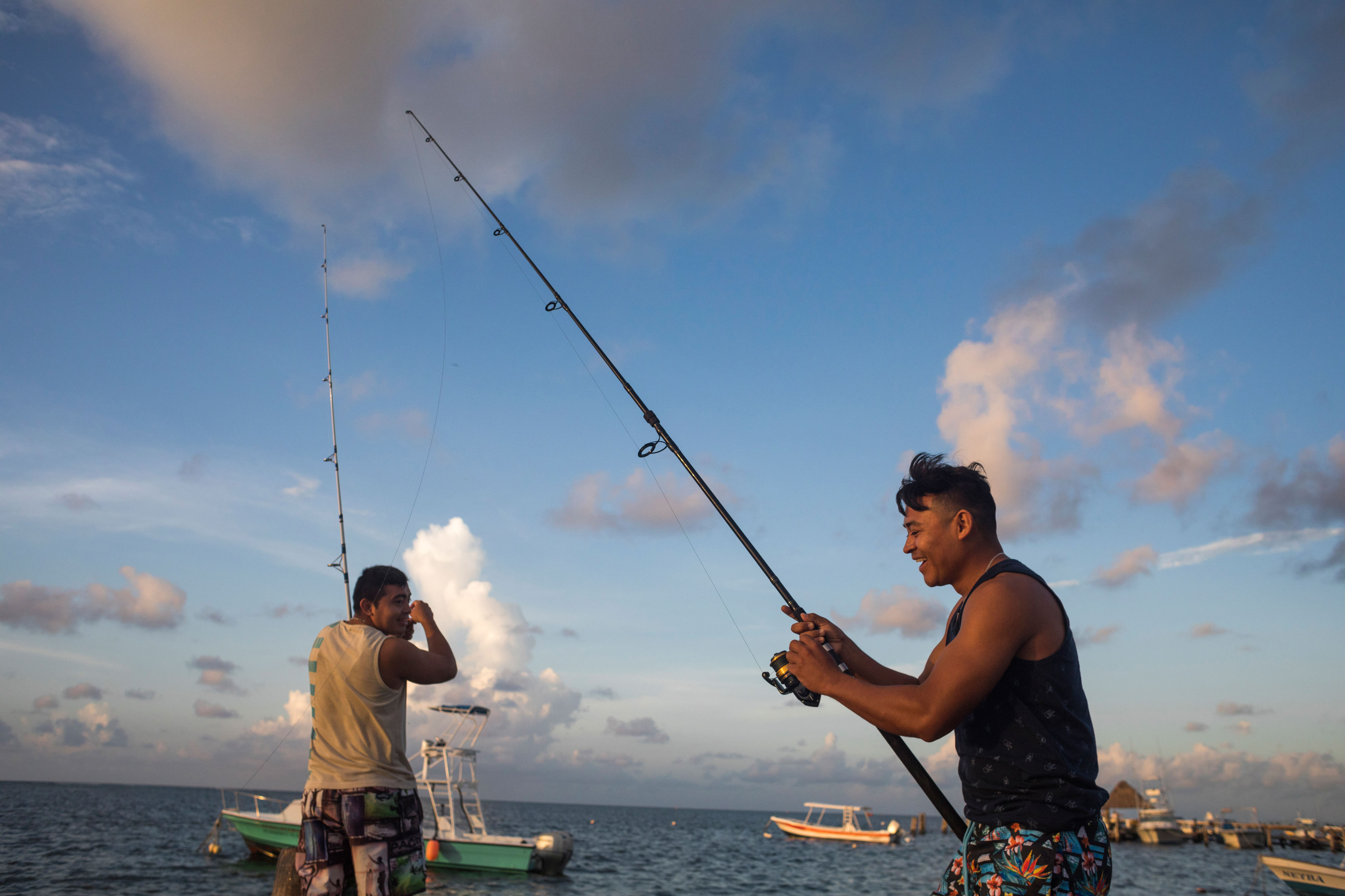 Two men are laughing as they fish with fishing poles from a pier.