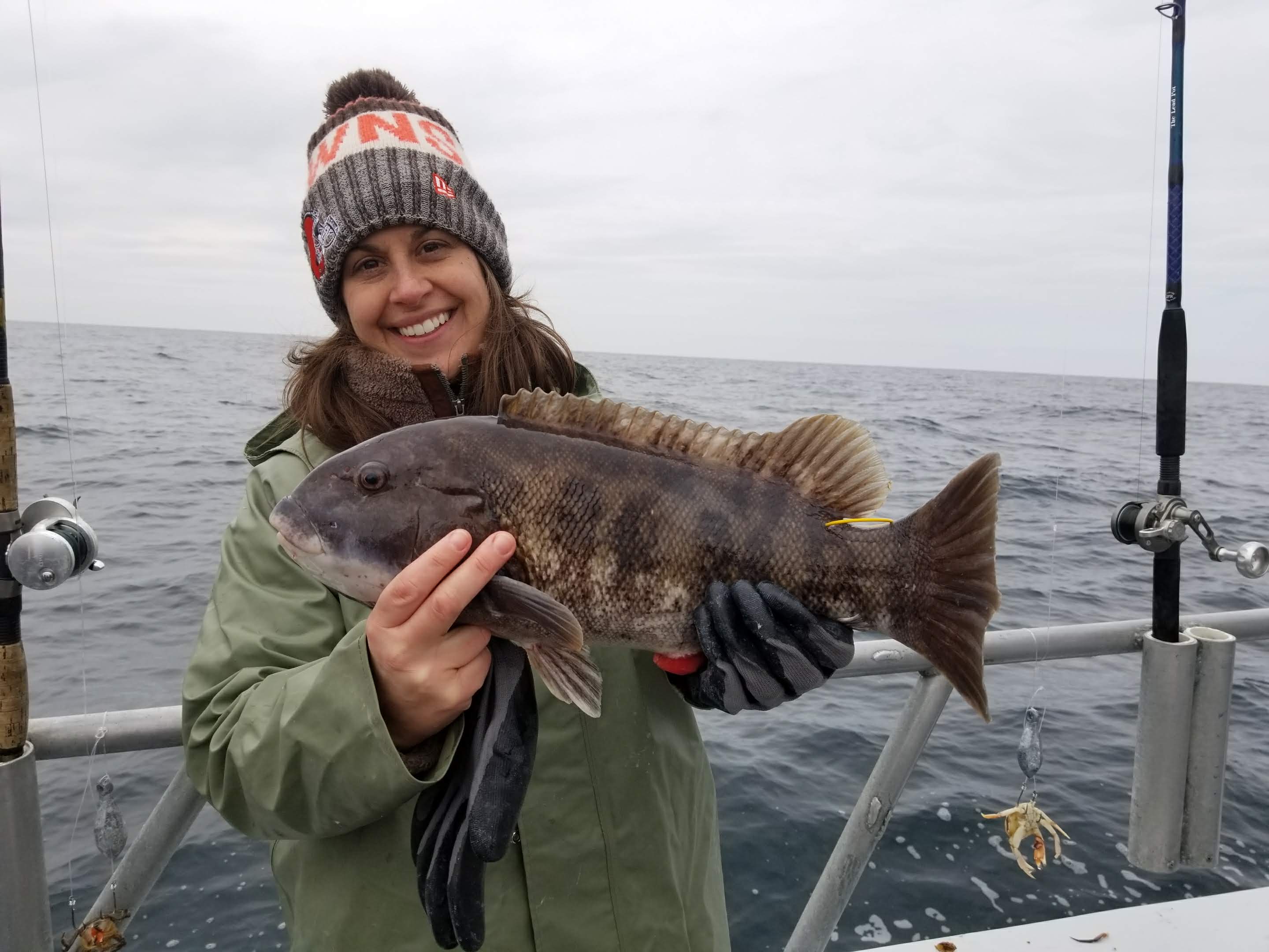 Virginia Fisheries Scientist Kate Wilke poses on a boat while holding a brown-striped fish.
