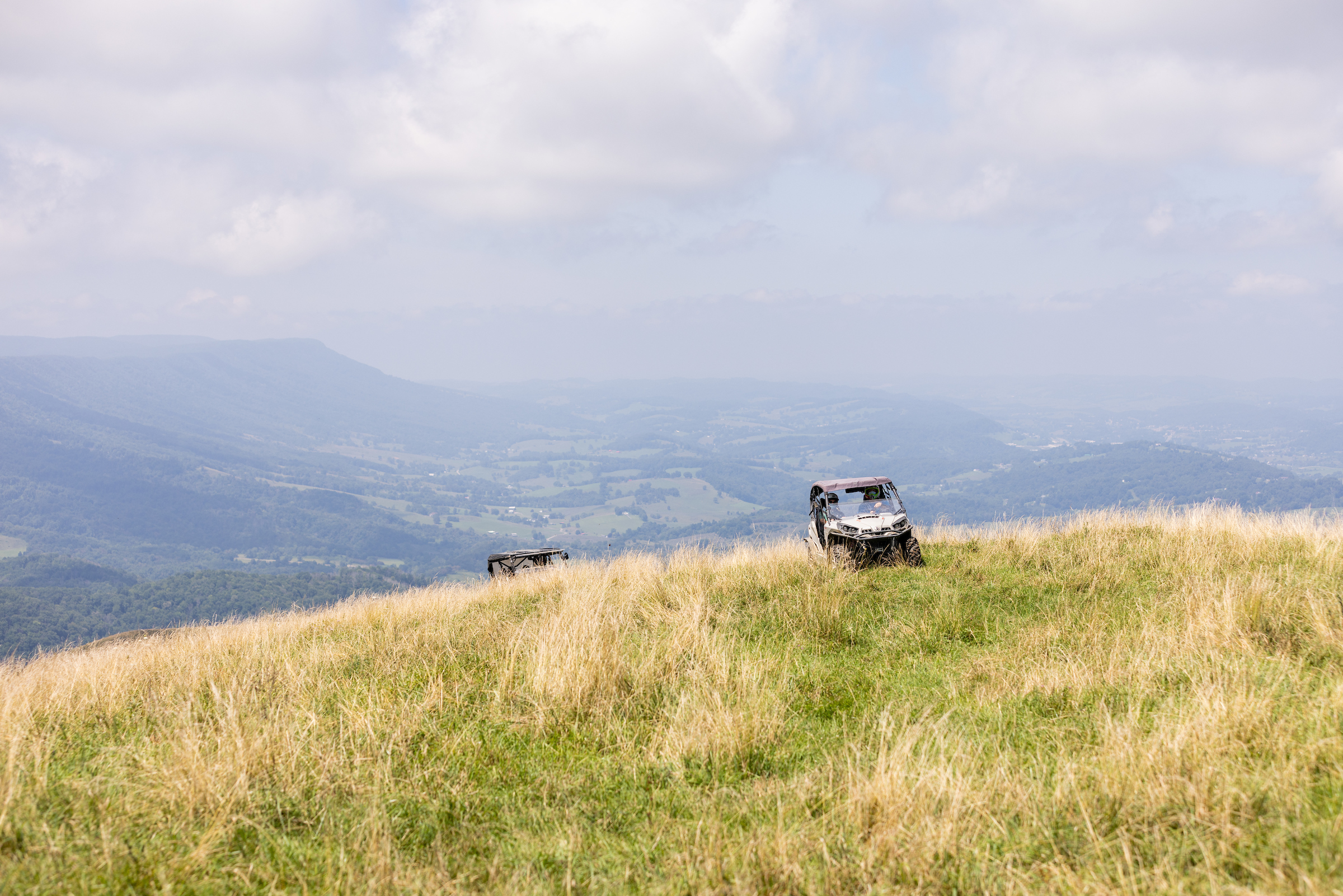 Two utility terrain vehicles crest the rise of one of the ridges on Beartown Mountain. A wide open valley spreads out below them.