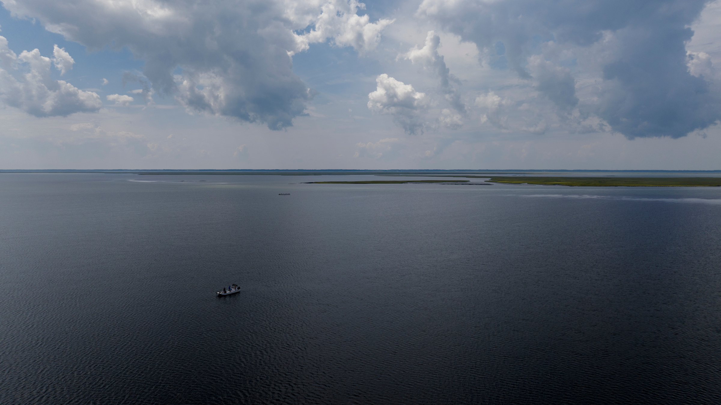 Aerial drone view looking down on a small skiff. The boat is a small speck in the wide expanse of a coastal Atlantic bay. 
