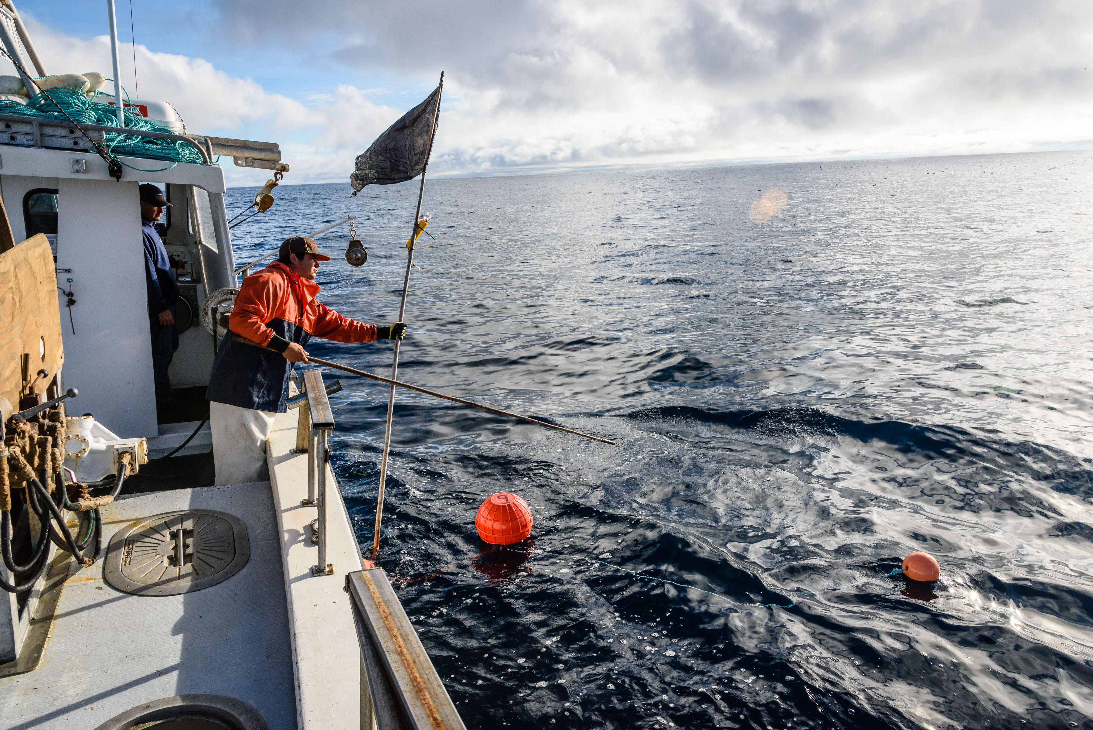 A fisherman holds a flag off the side of a fishing boat as part of fisheries testing.