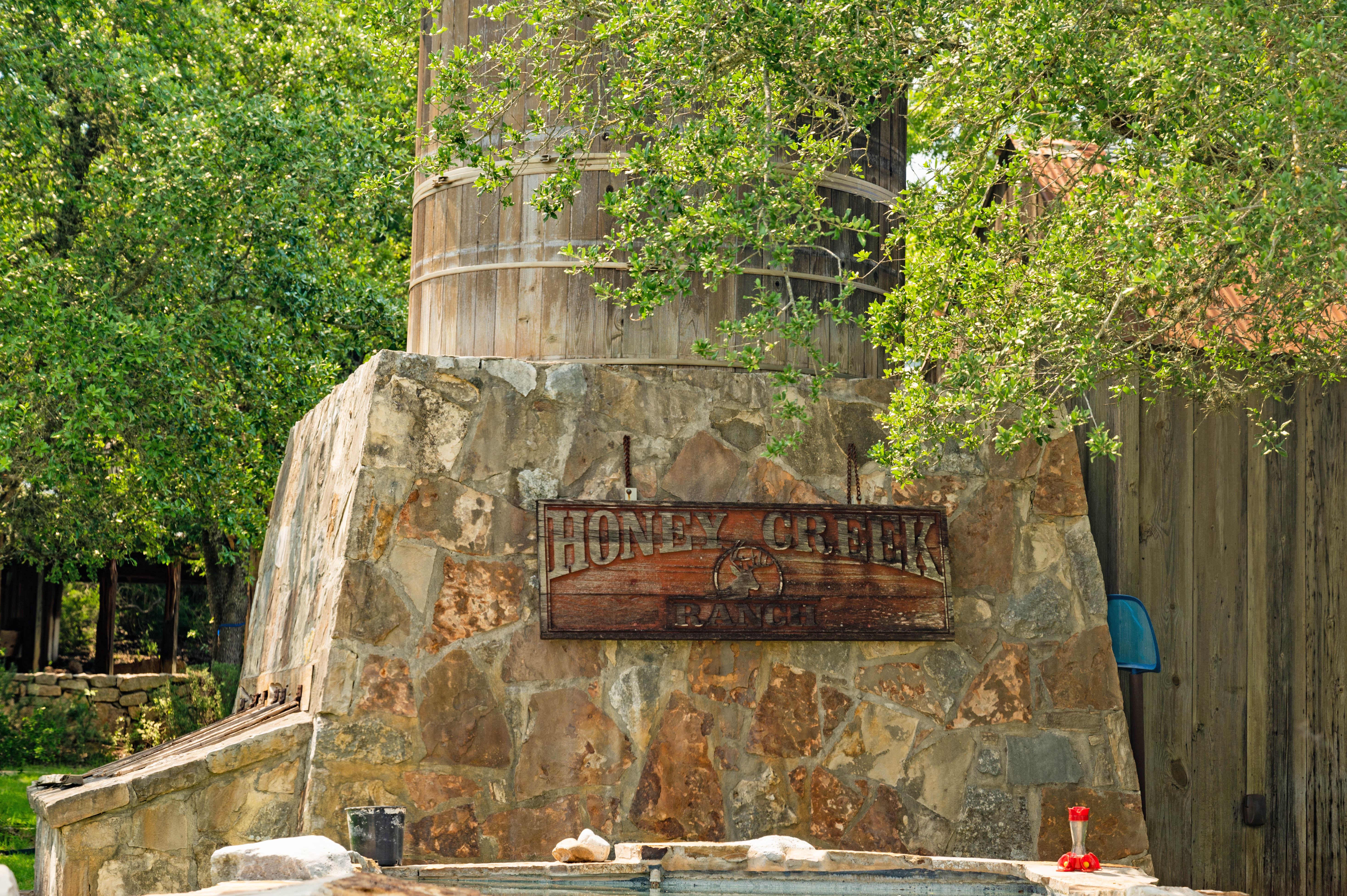 A wooden water tank surrounded by stone with a sign reading Honey Creek Ranch.