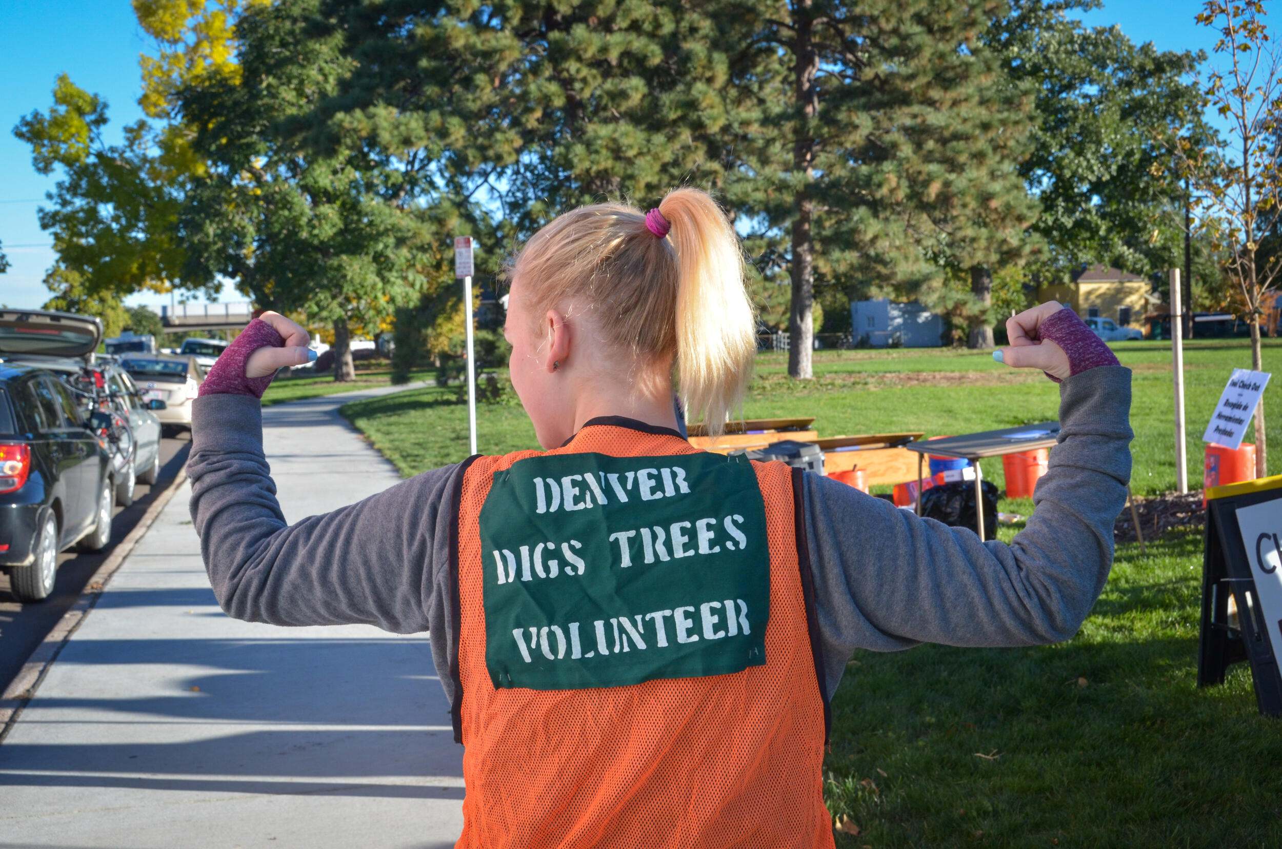 A woman wearing a construction vest flexing her strong arms.