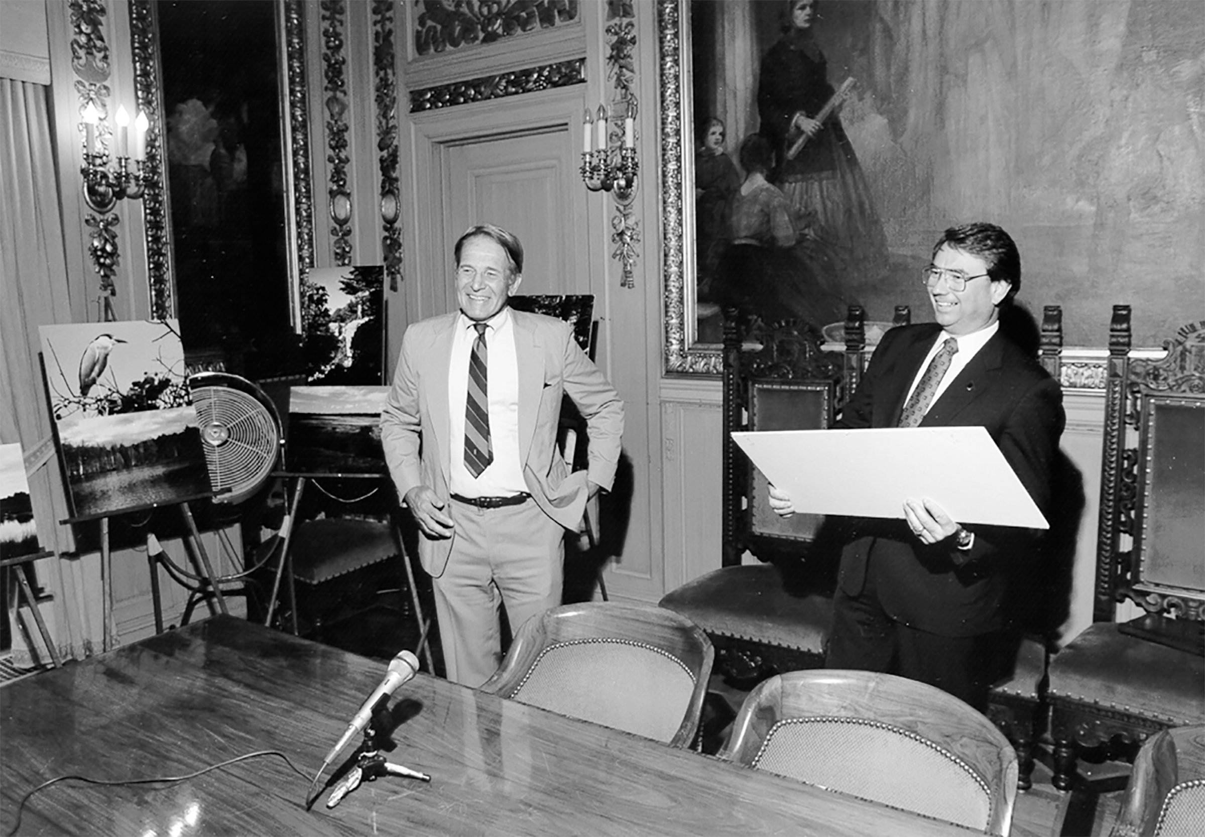 A black and white photo of two people smiling in a board room. 