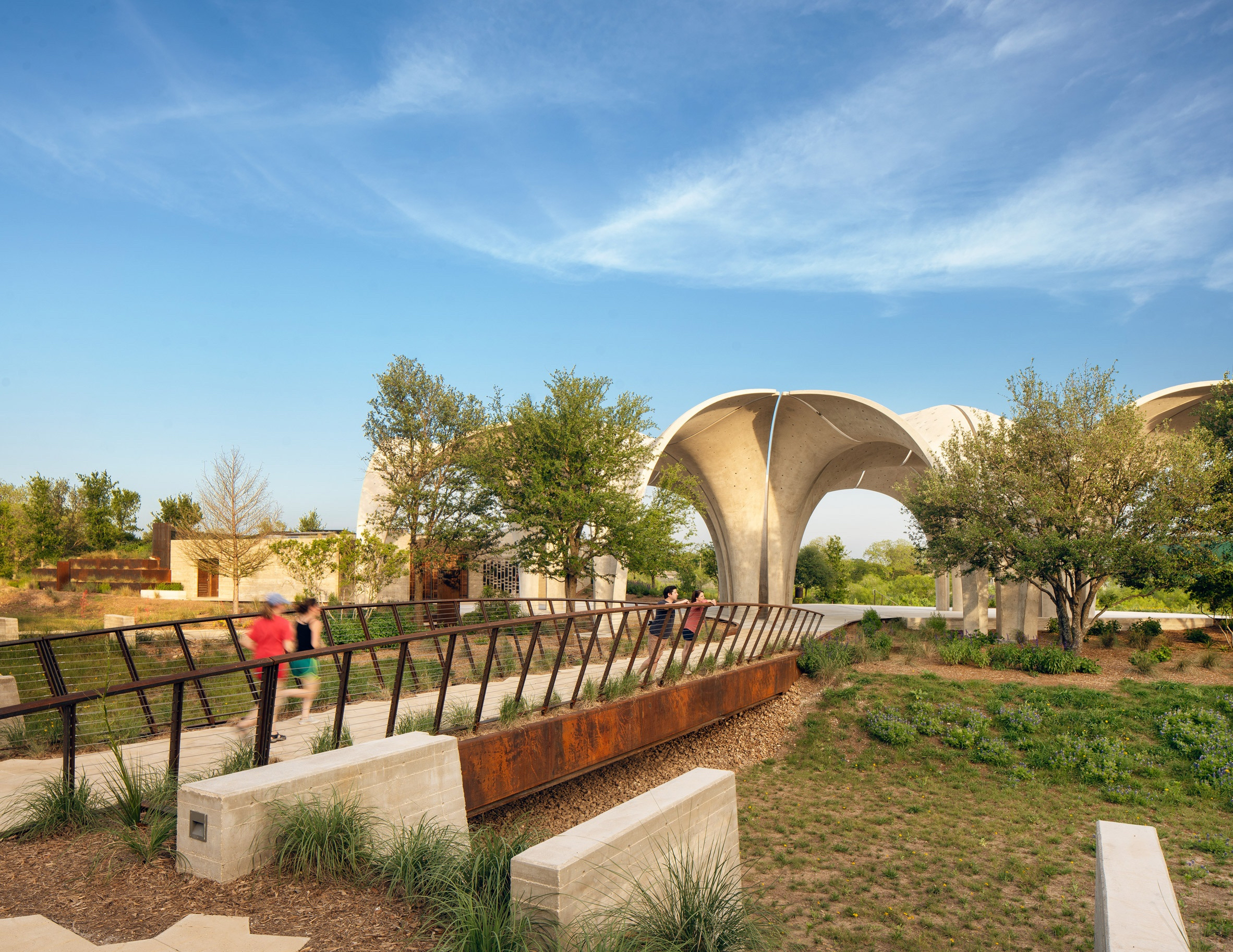 Four people explore a green park with a bridge and a limestone structure in the center.