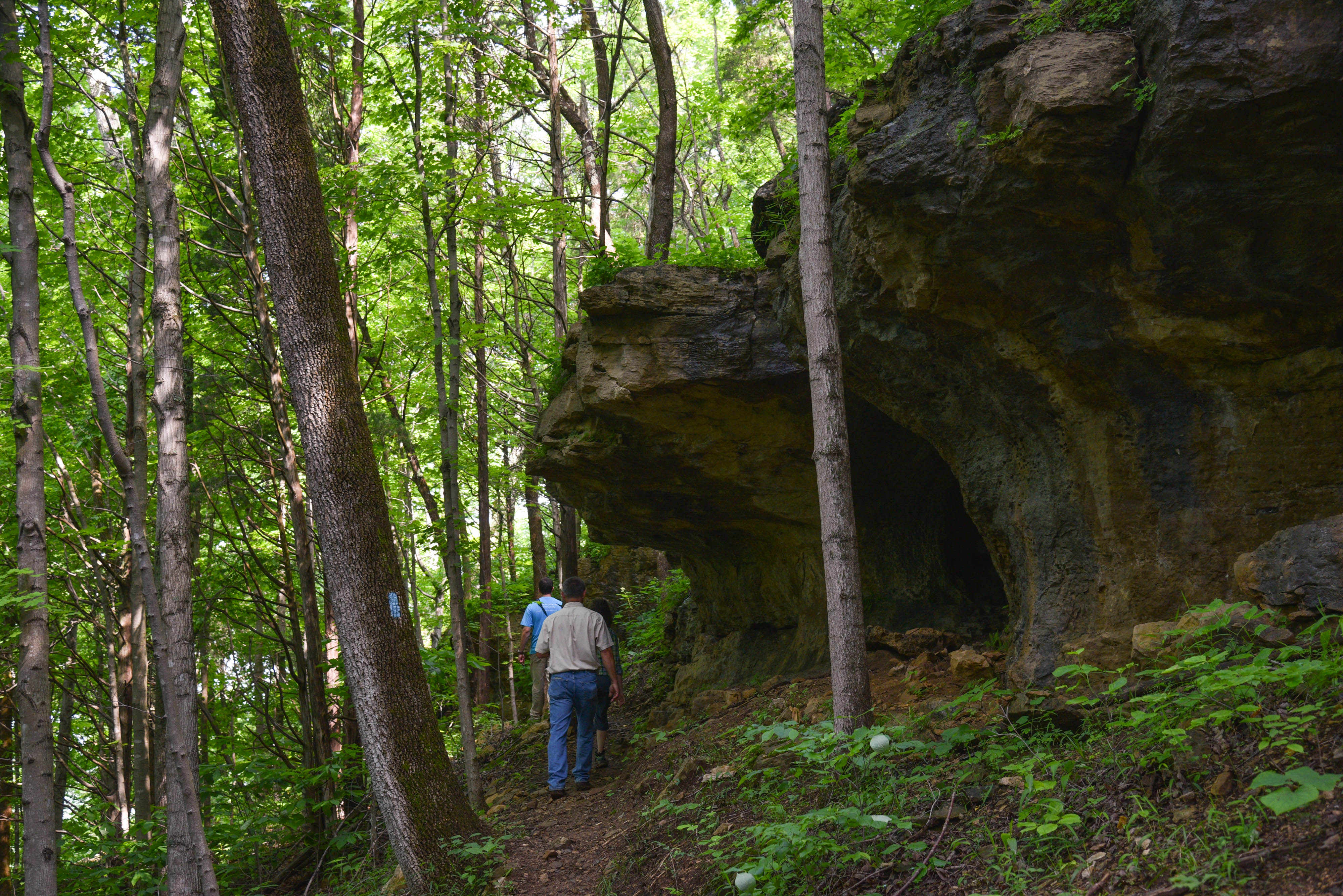 Hikers stand under large rocks in the woods.