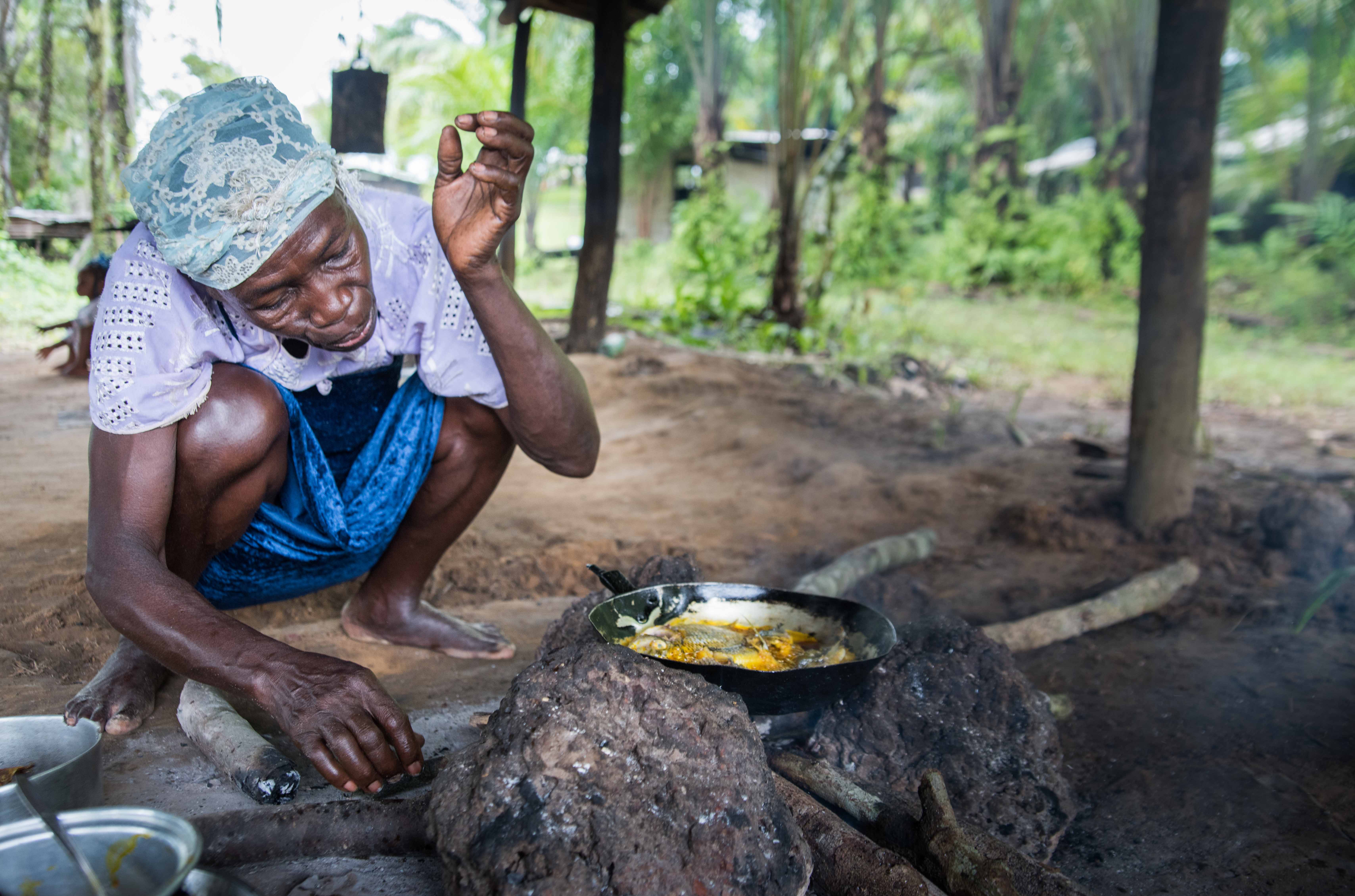 Woman crouches next to cooking fish