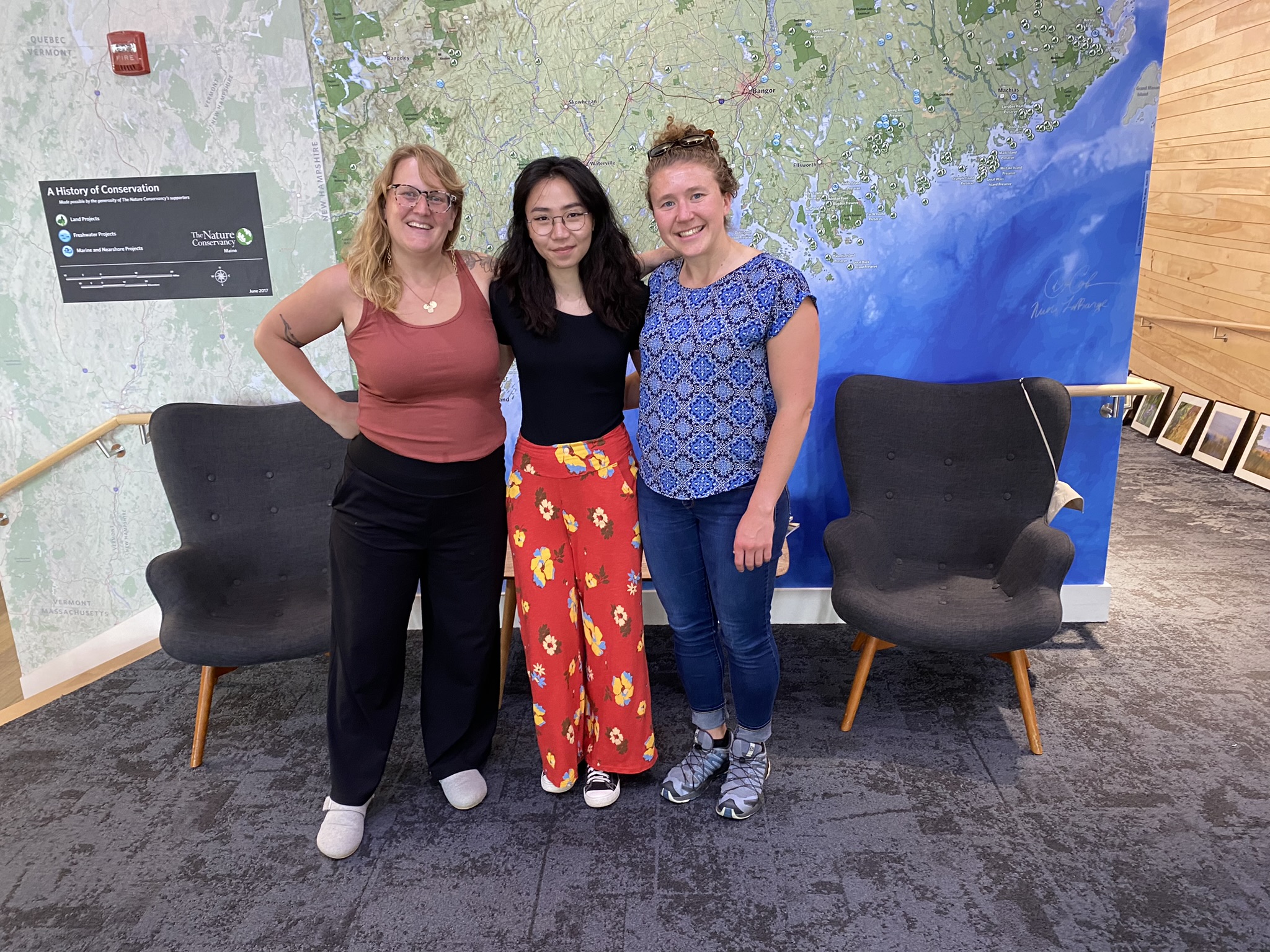 Maggie Stone, Marla Ganbat and Hadley Couraud pose in front of a large map of Maine.