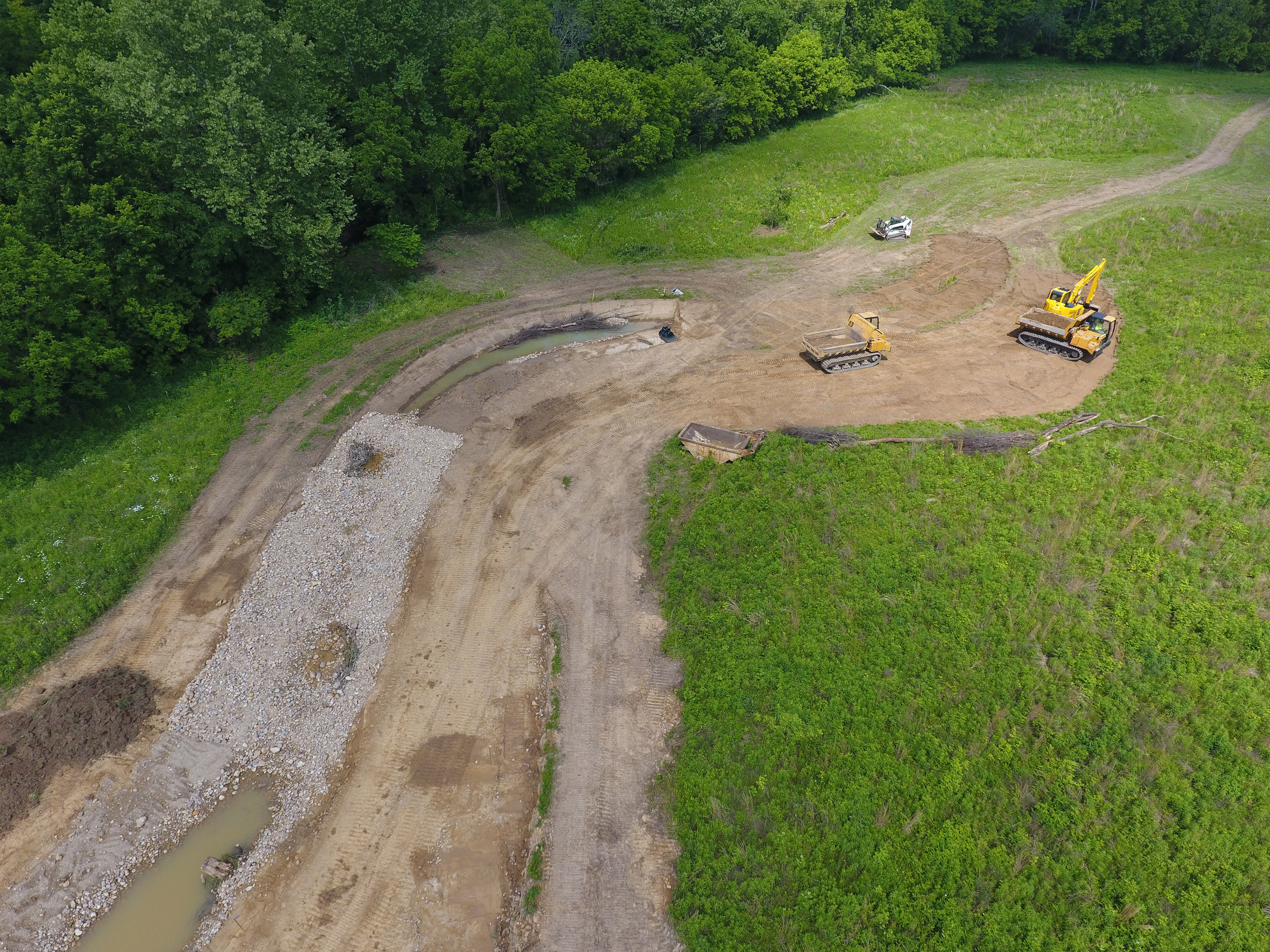 Construction crews work to dig new stream bed near forest.