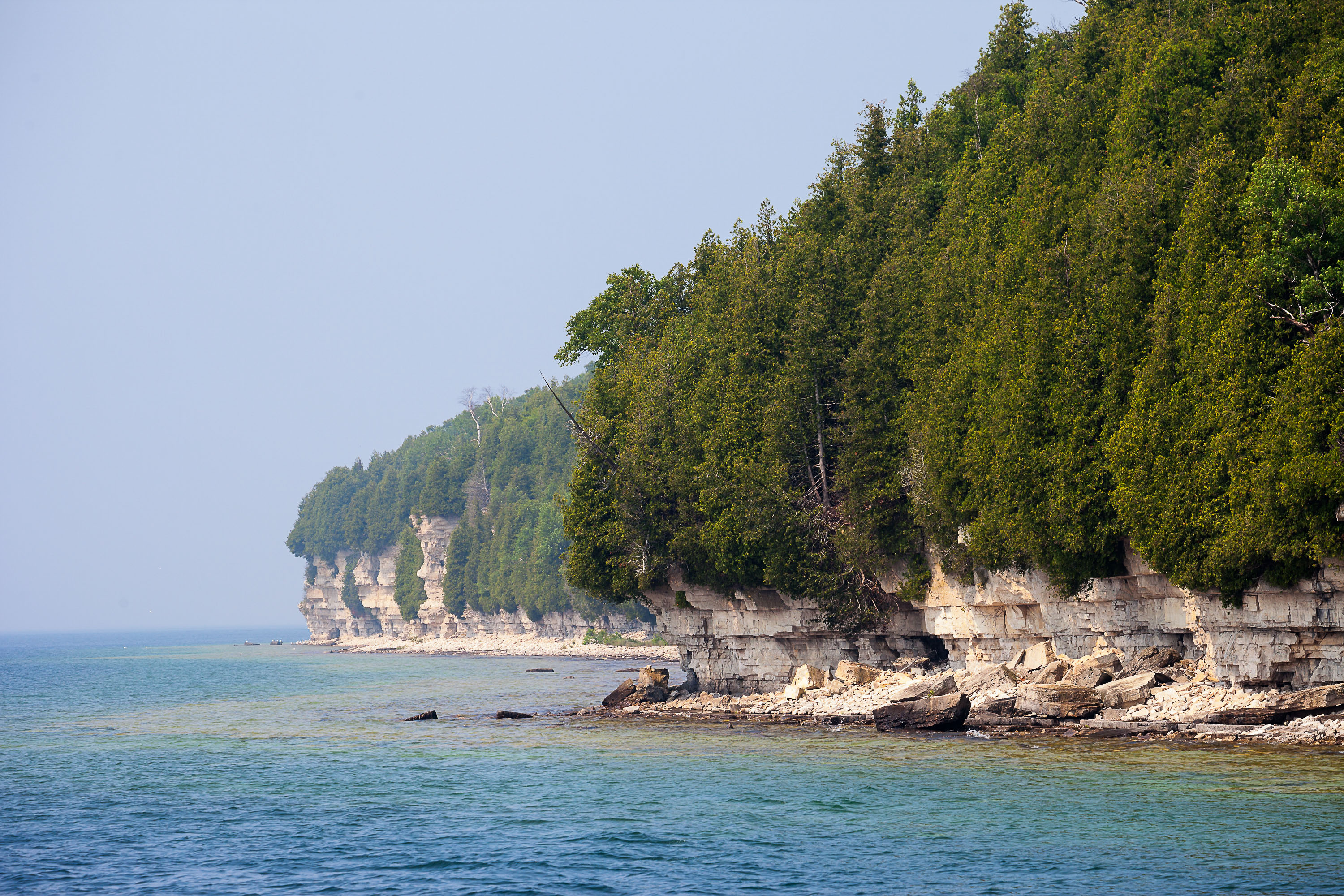 A rocky shoreline with conifer trees along Lake Michigan. 