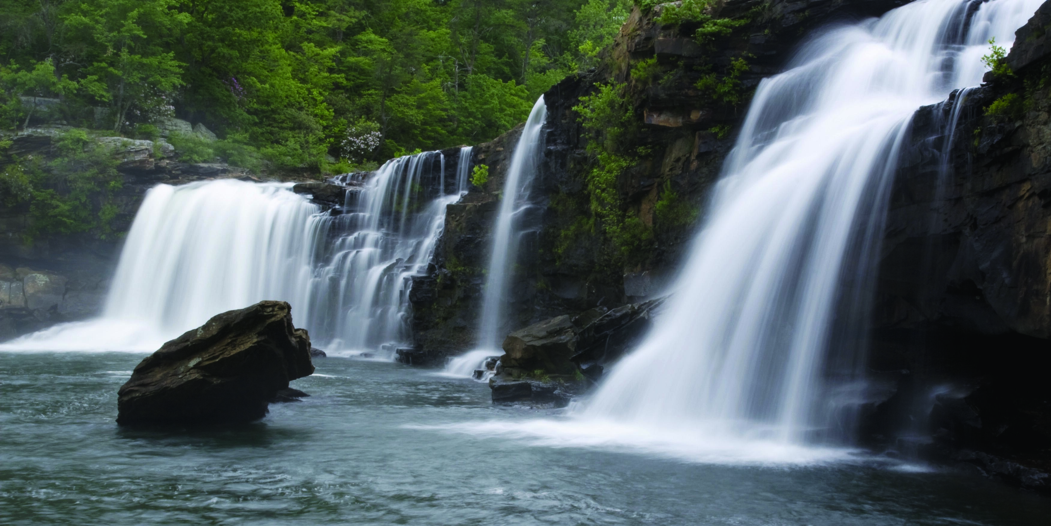  A wall of rock with a dramatic series of waterfalls flowing into a waterbody below.