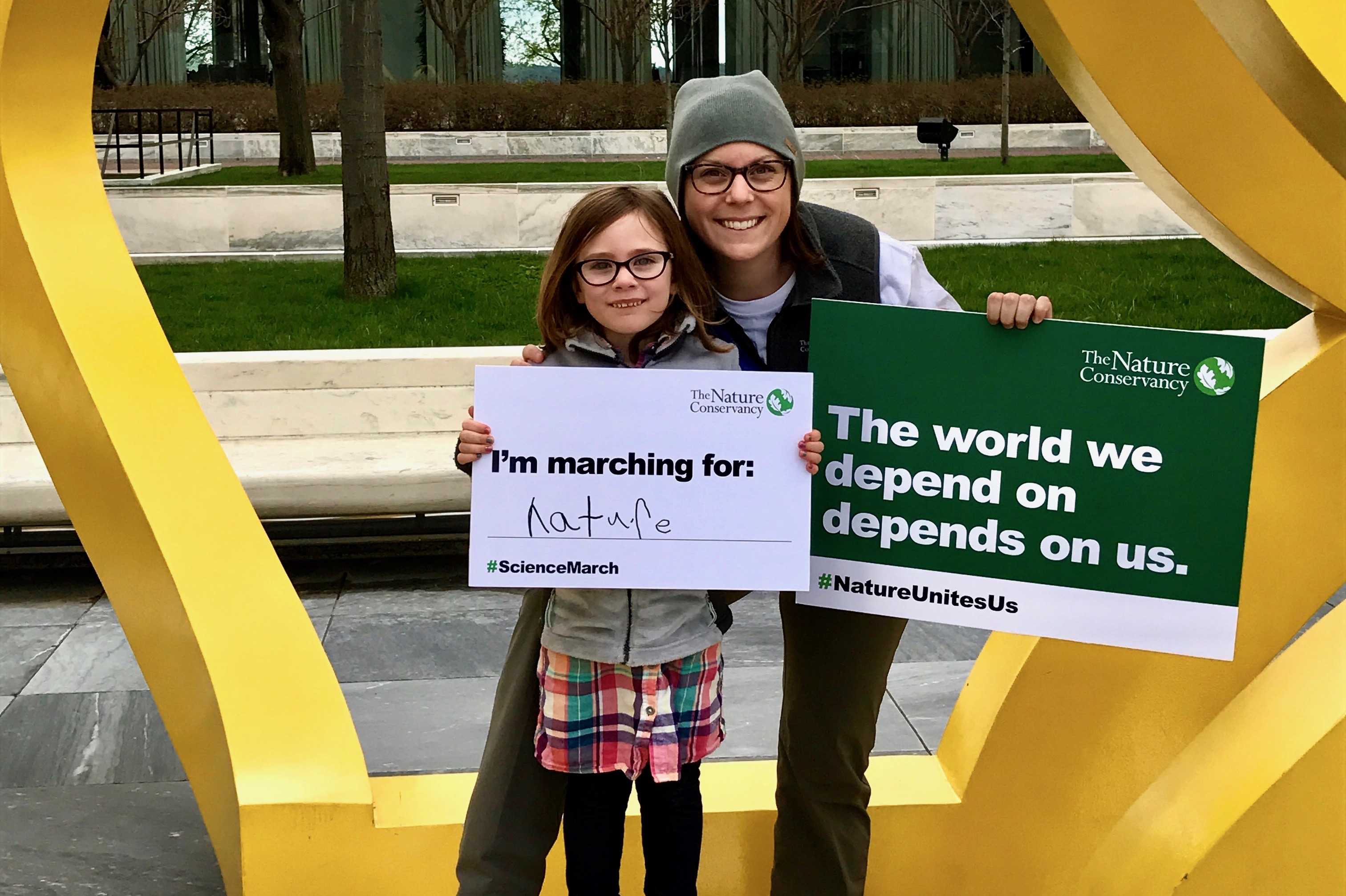 A woman at right with a sign in her hand saying "The world we depend on depends on us." next to a younger individual holding a sign saying "I'm marching for nature."