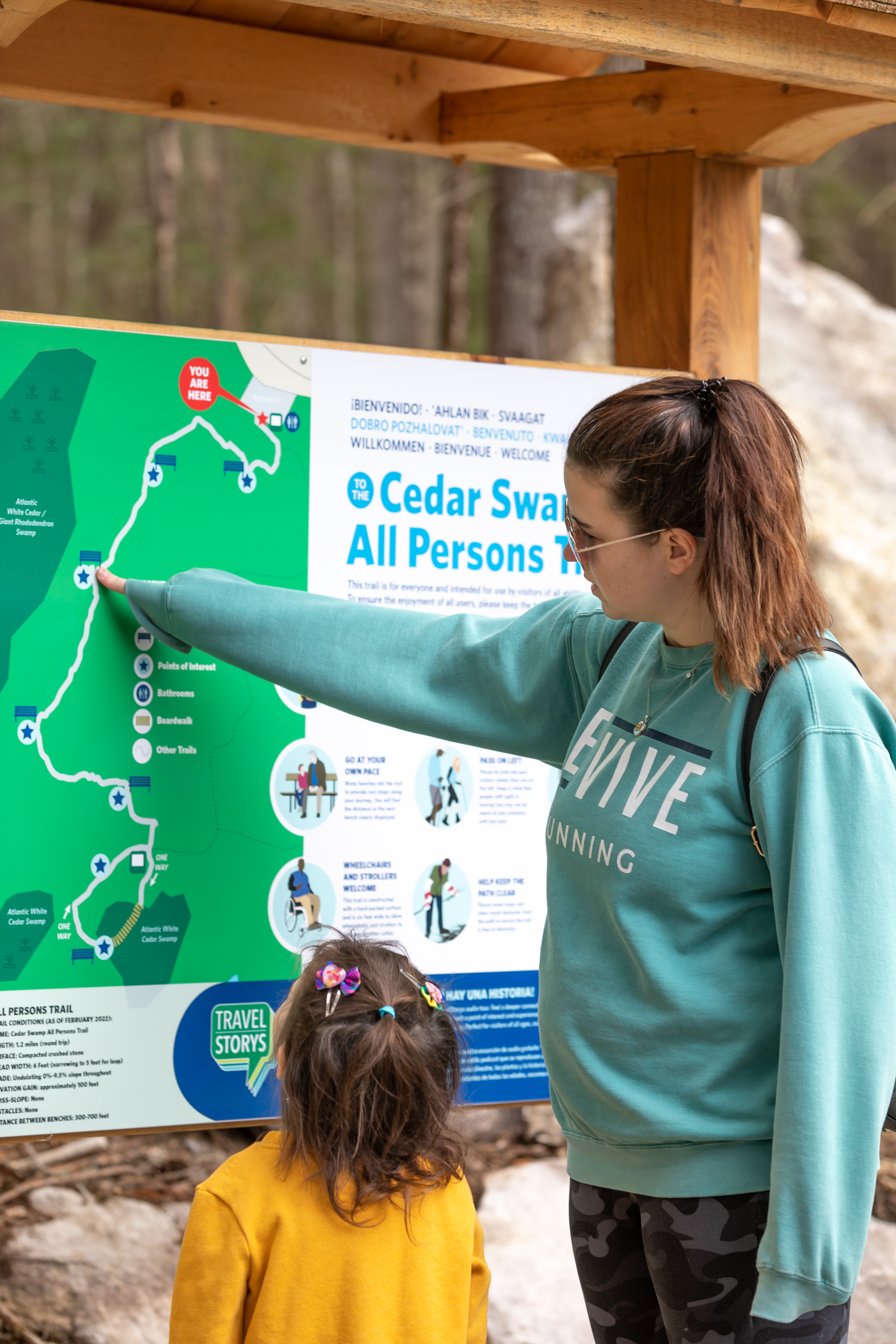 A woman points to an outdoor map while a small child looks on.