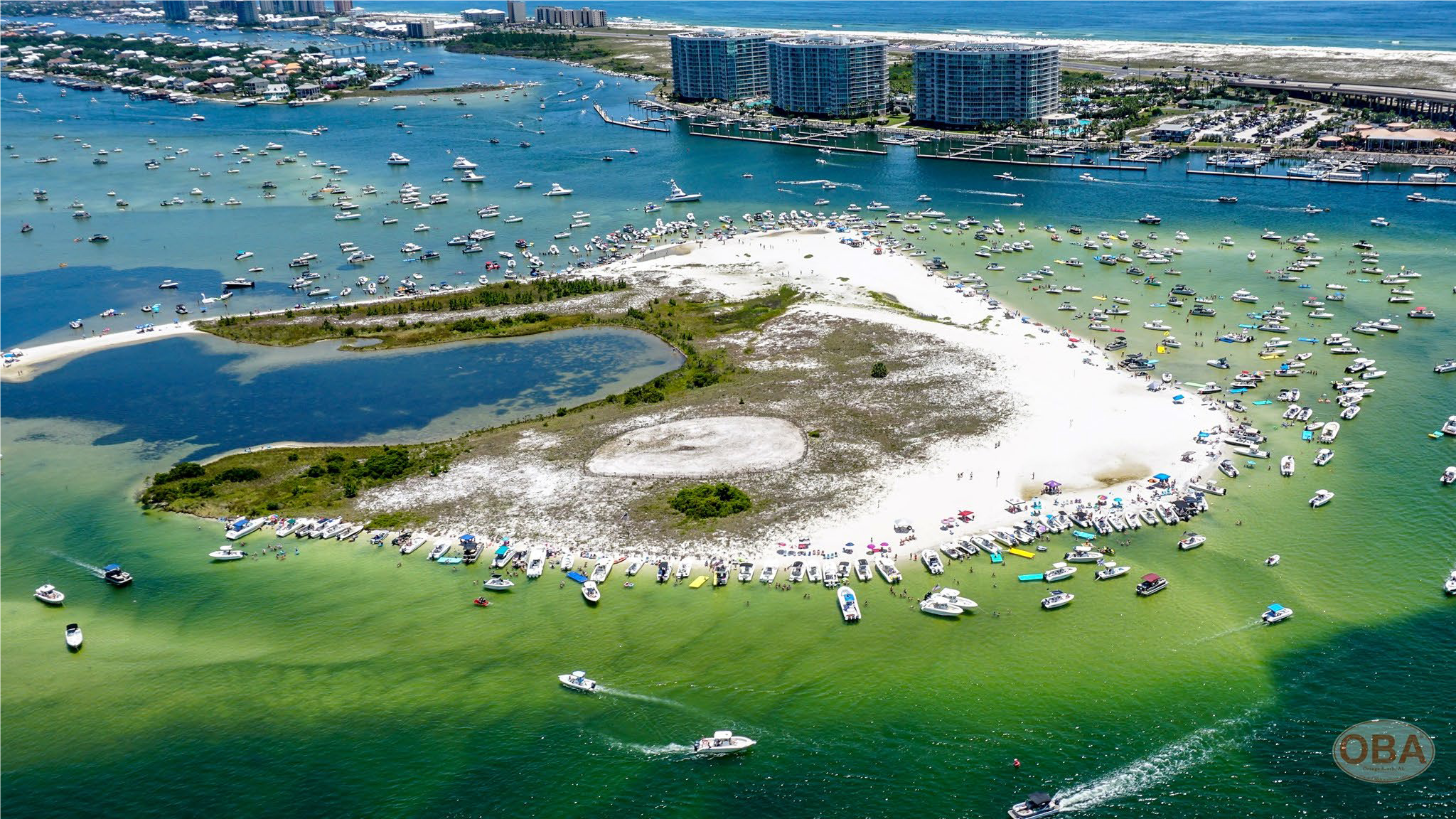 Aerial view of a small sandy island surrounded by turquoise water crowded with boats.