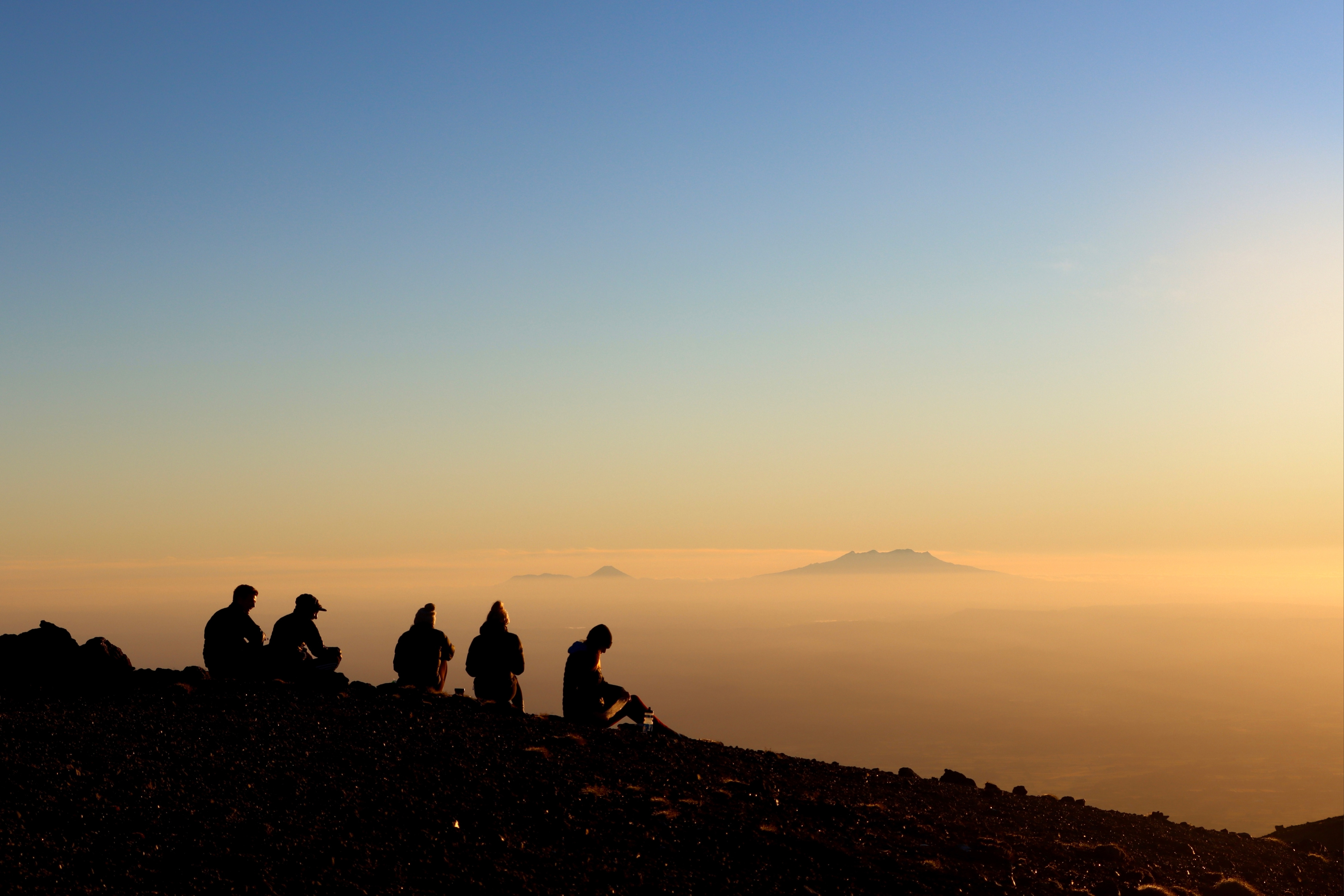 A group of people sit on a peak at sunrise.