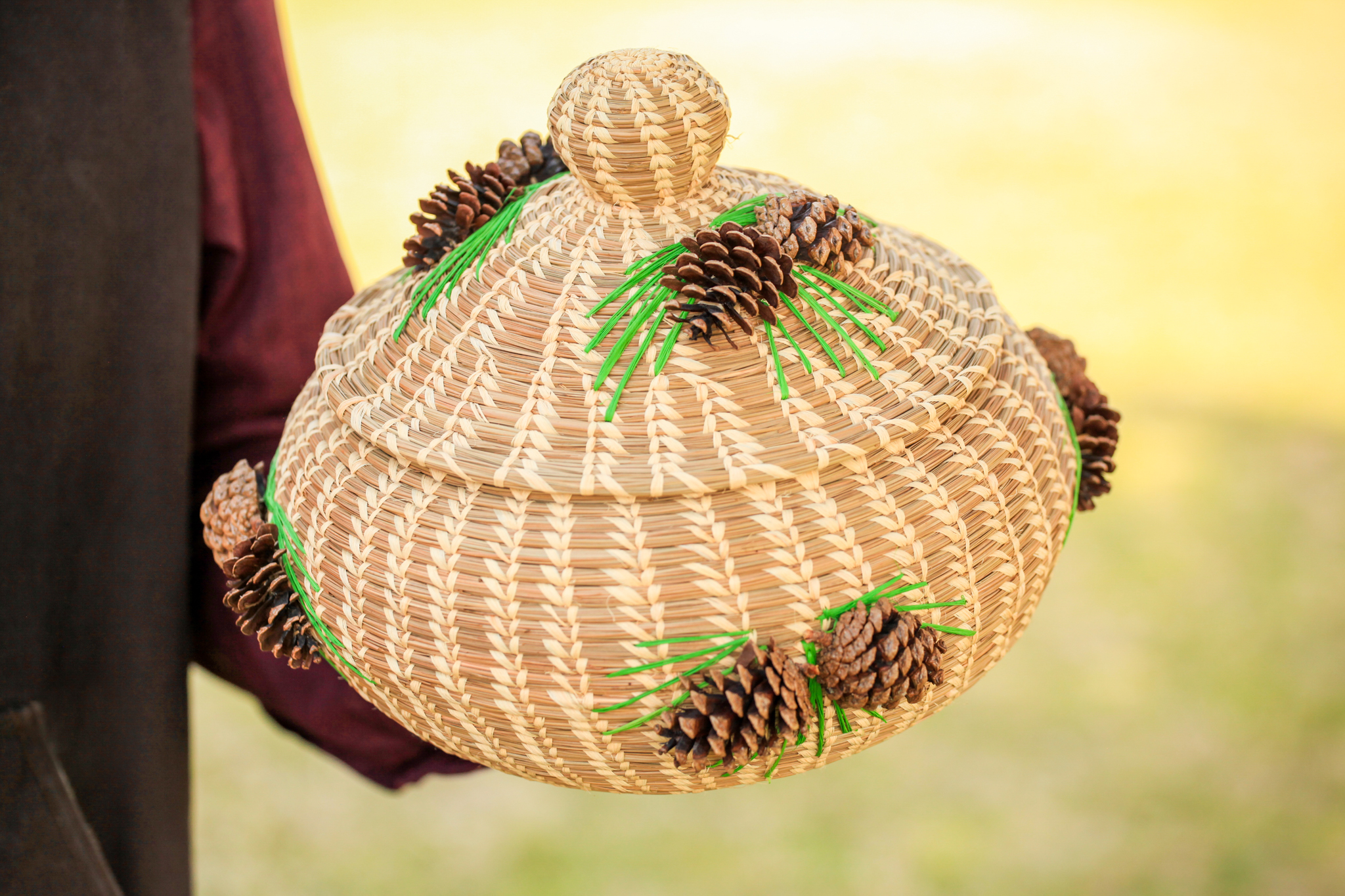 A brown woven basket adorned with bright green raffia and pinecones.