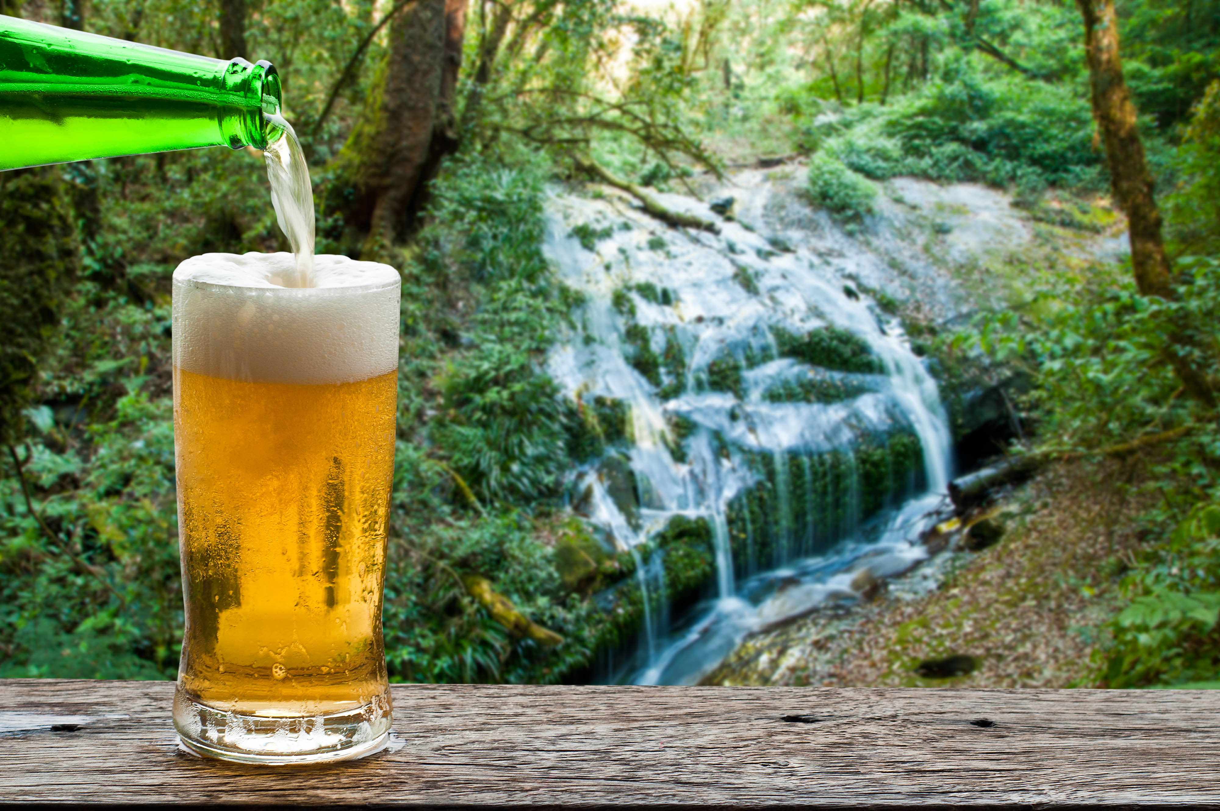 Beer glass sits on a table next to a waterfall.