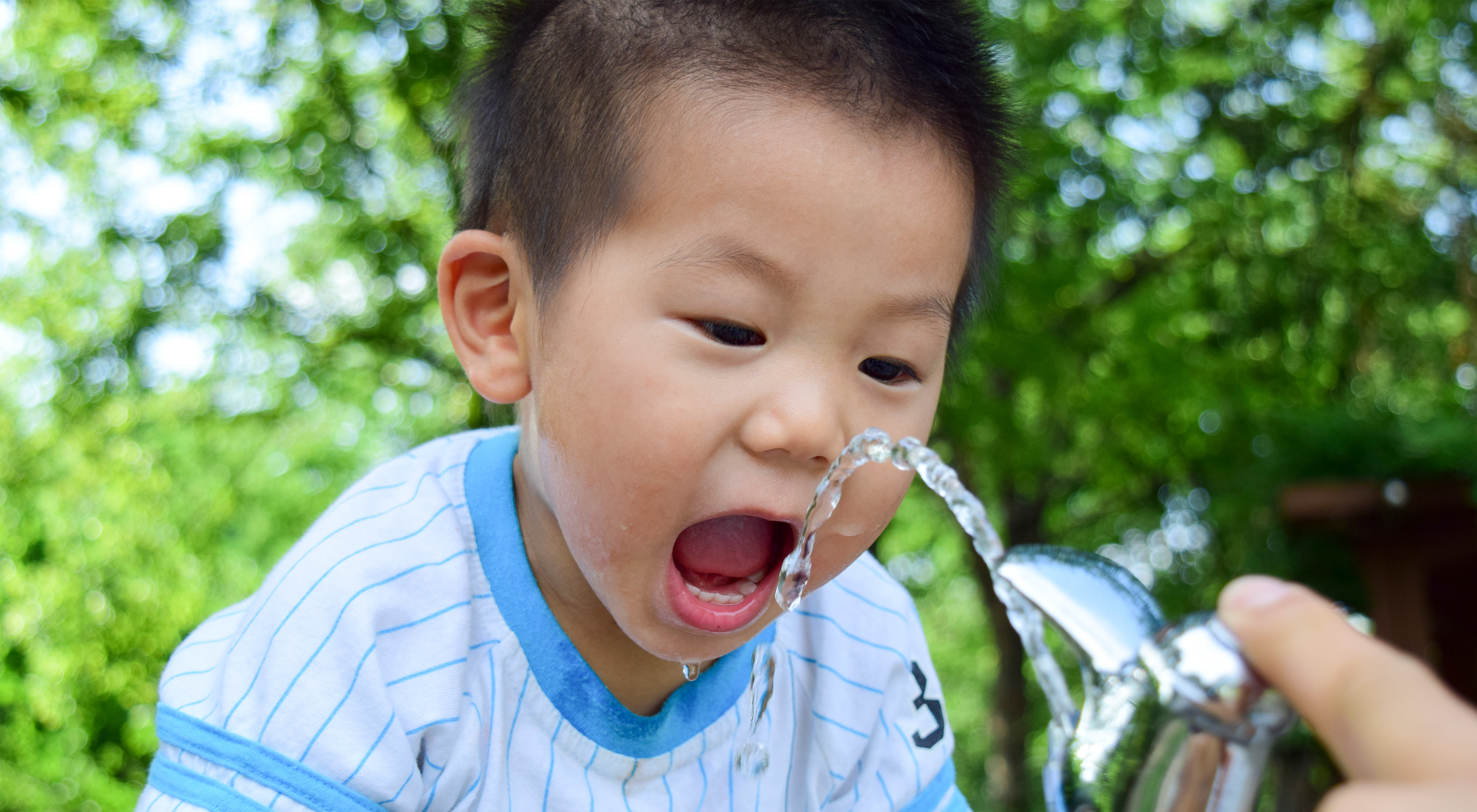 A boy drinks water out of a fountain.