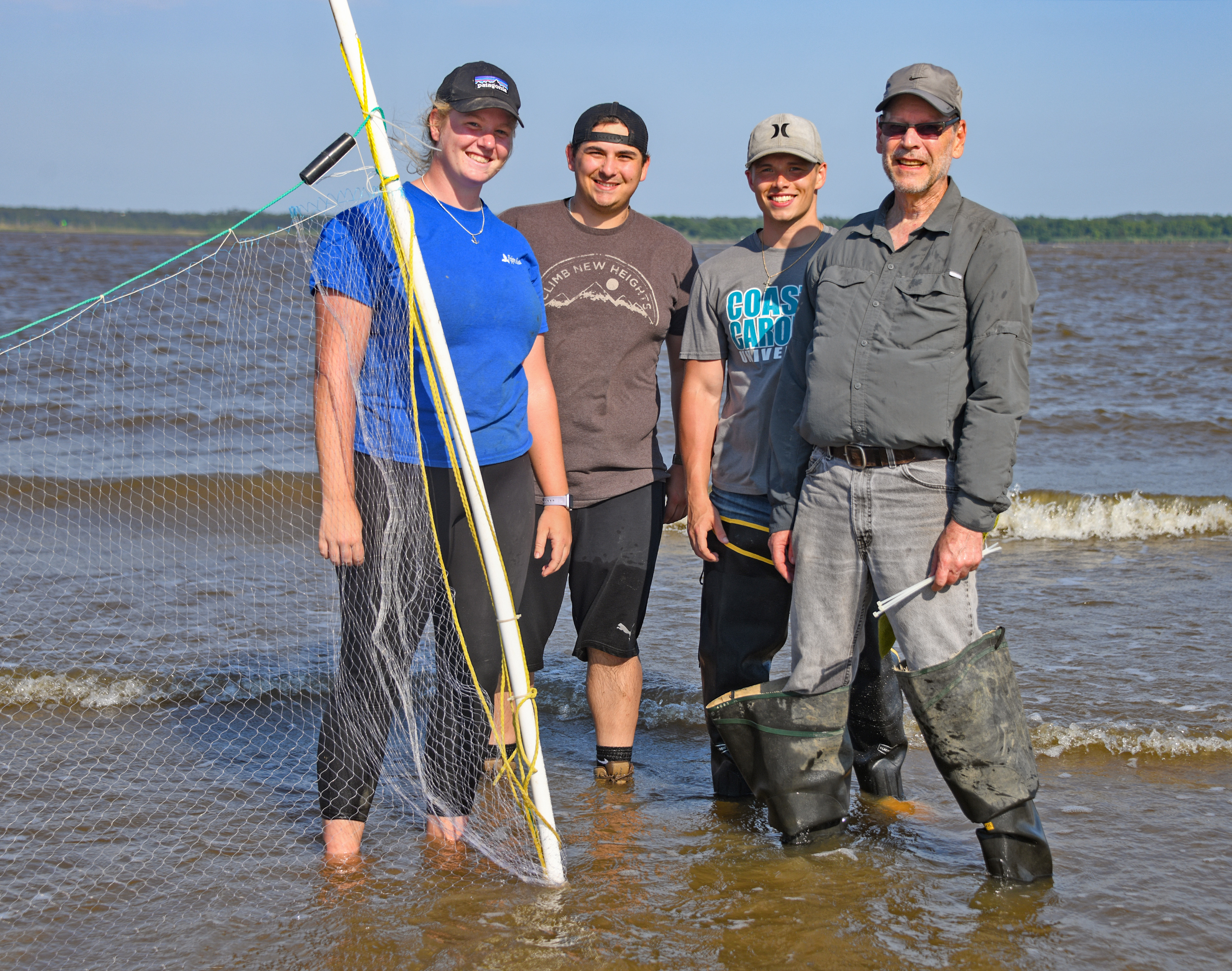 Four researchers stand in the surf.