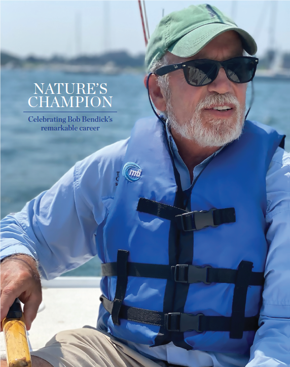 A man wearing a hat, sunglasses and a blue vest looks out at the ocean from a boat.