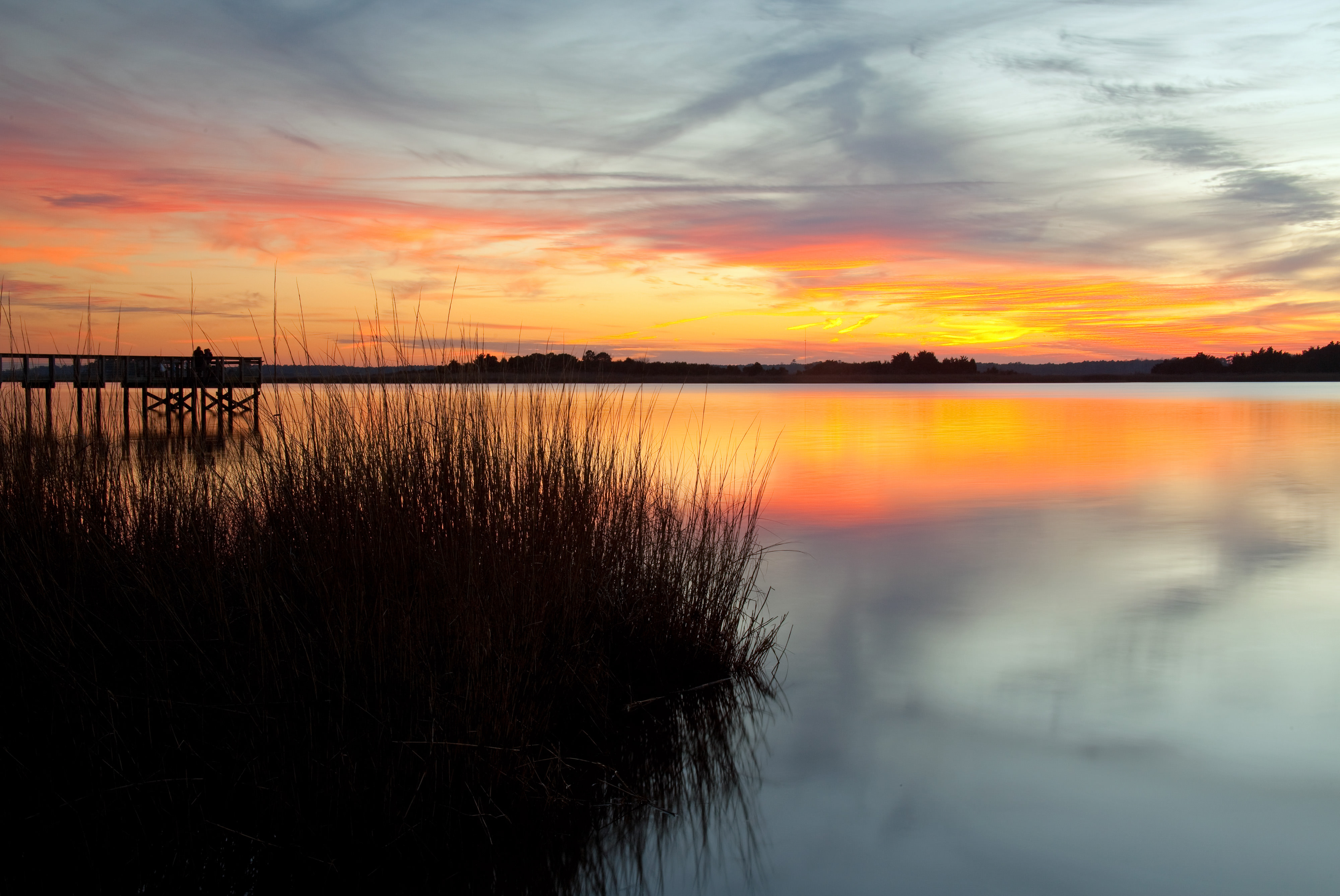 A sun sets over calm waters and a patch of grass.