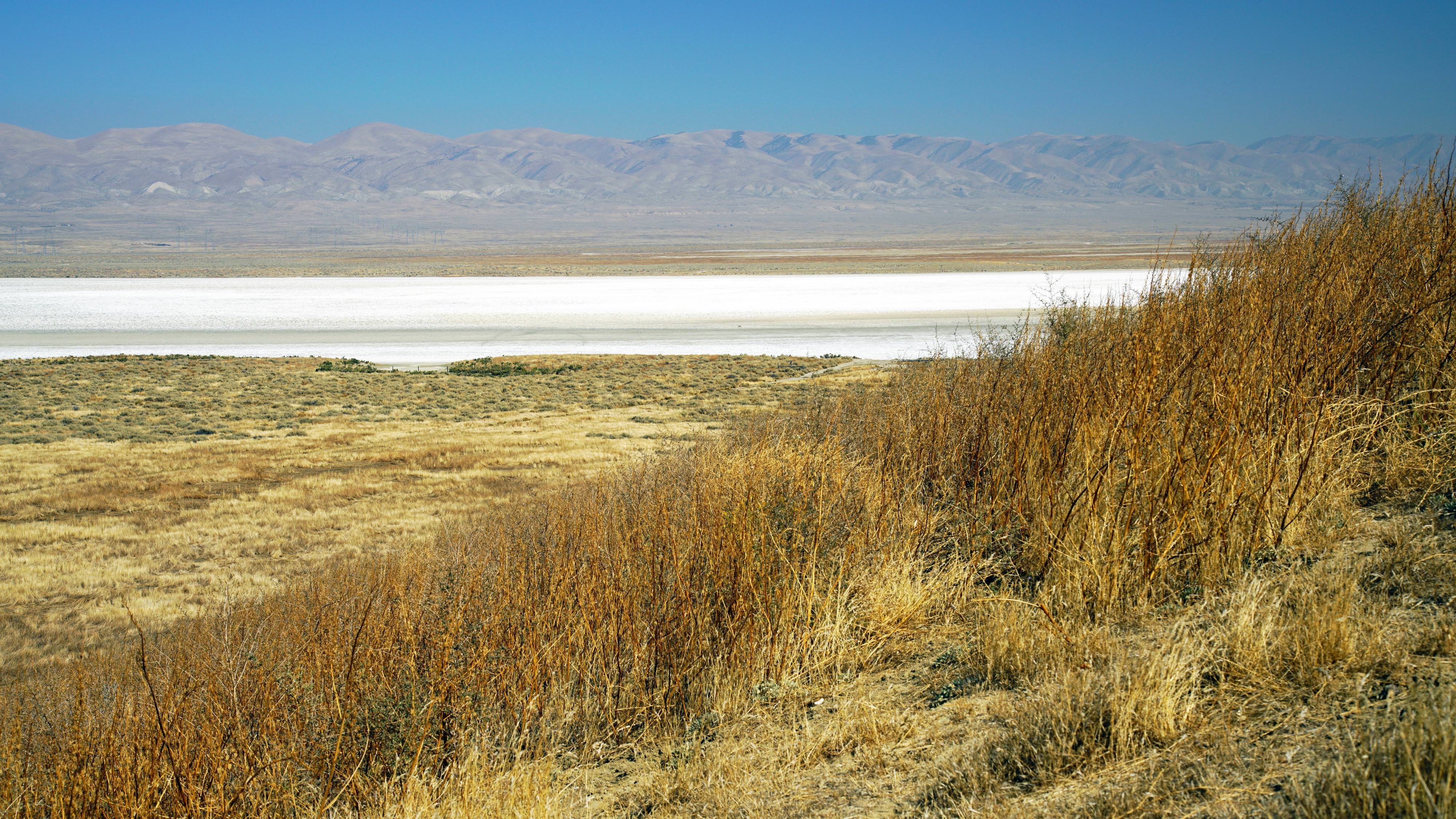 A white expanse of minerals on a dry lakebed with hills in the distance.