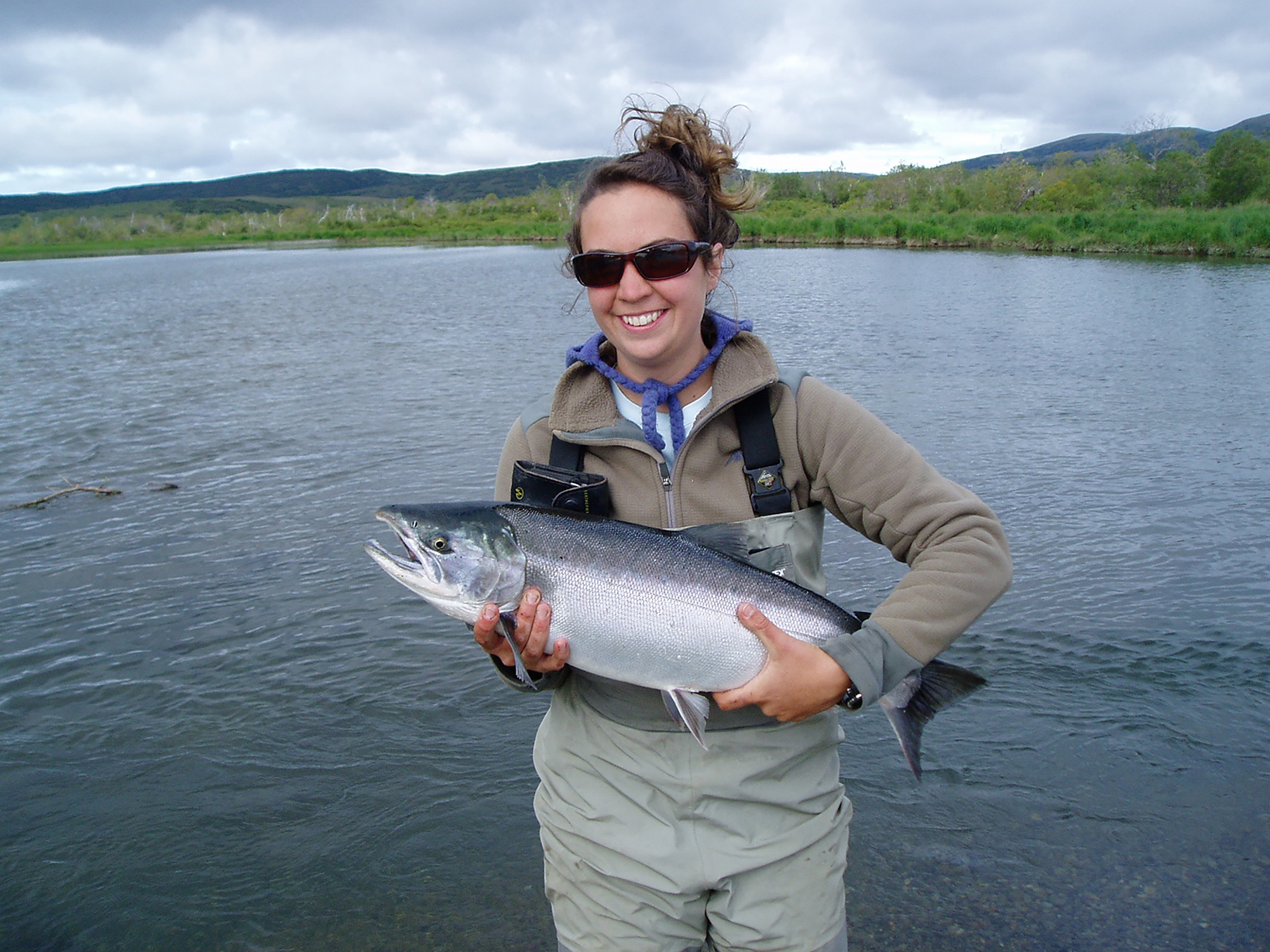 TNC scientist in Alaska's Bristol Bay holding a fish as she stands in a lake.