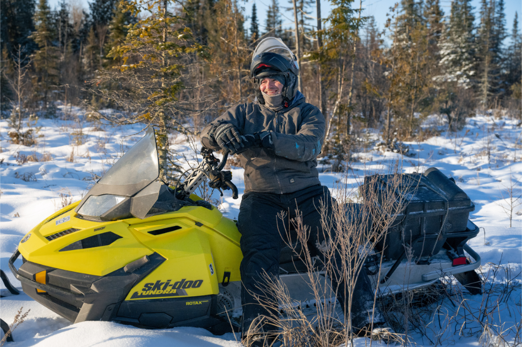 A smiling person wearing a helmet sits on a snowmobile.
