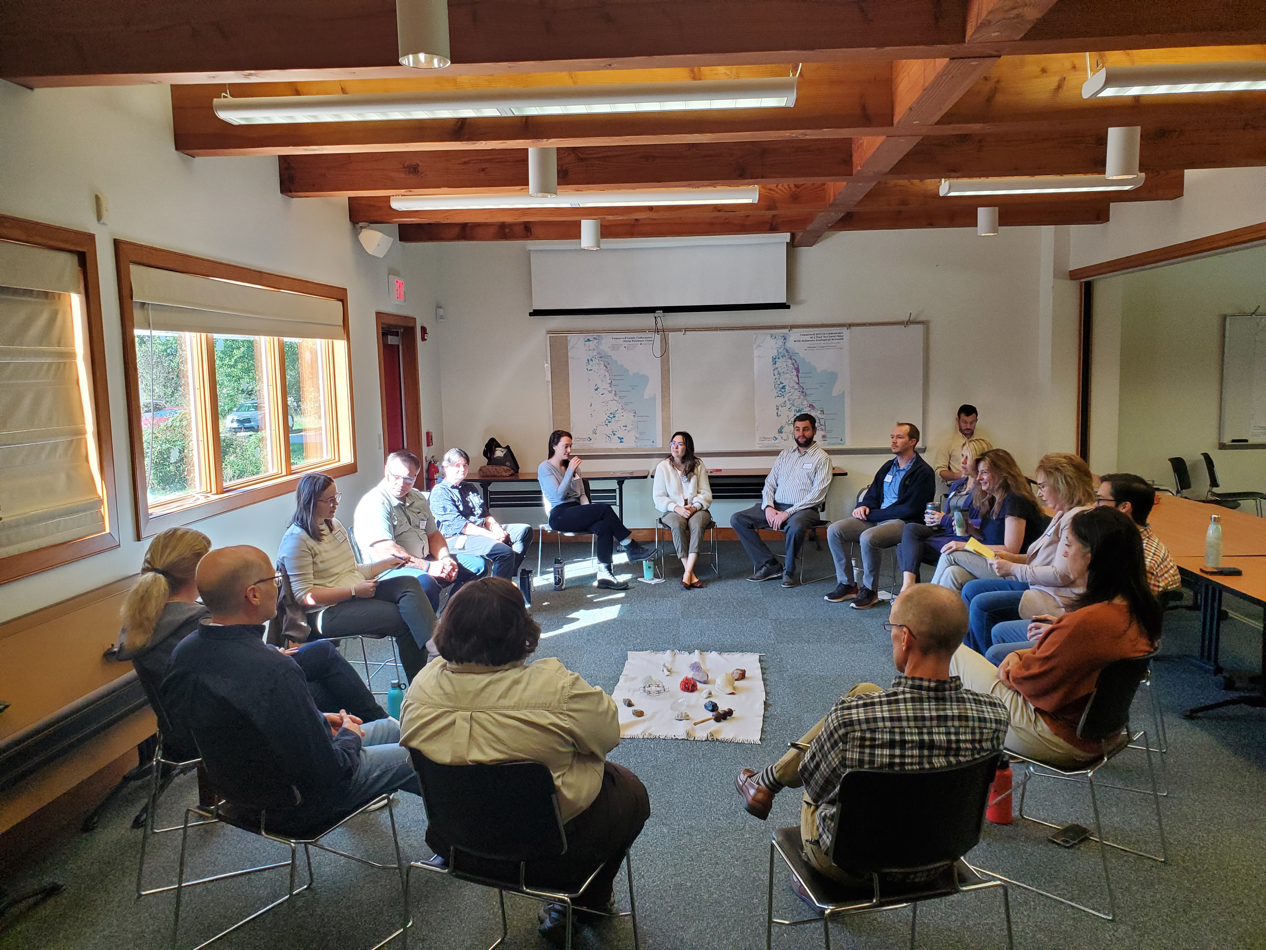 A group of people sit in chairs in a circle facing eachother. 