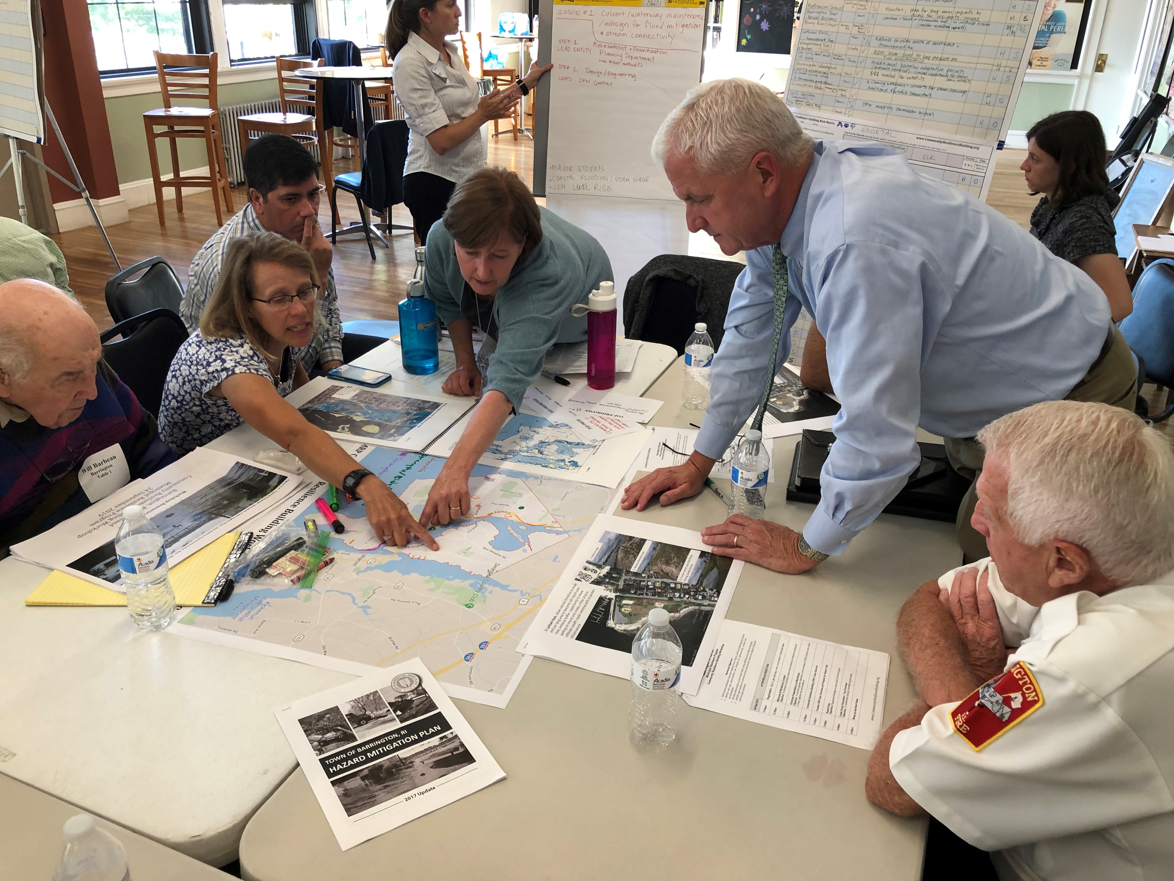 A group of people gather around a table to look at maps.