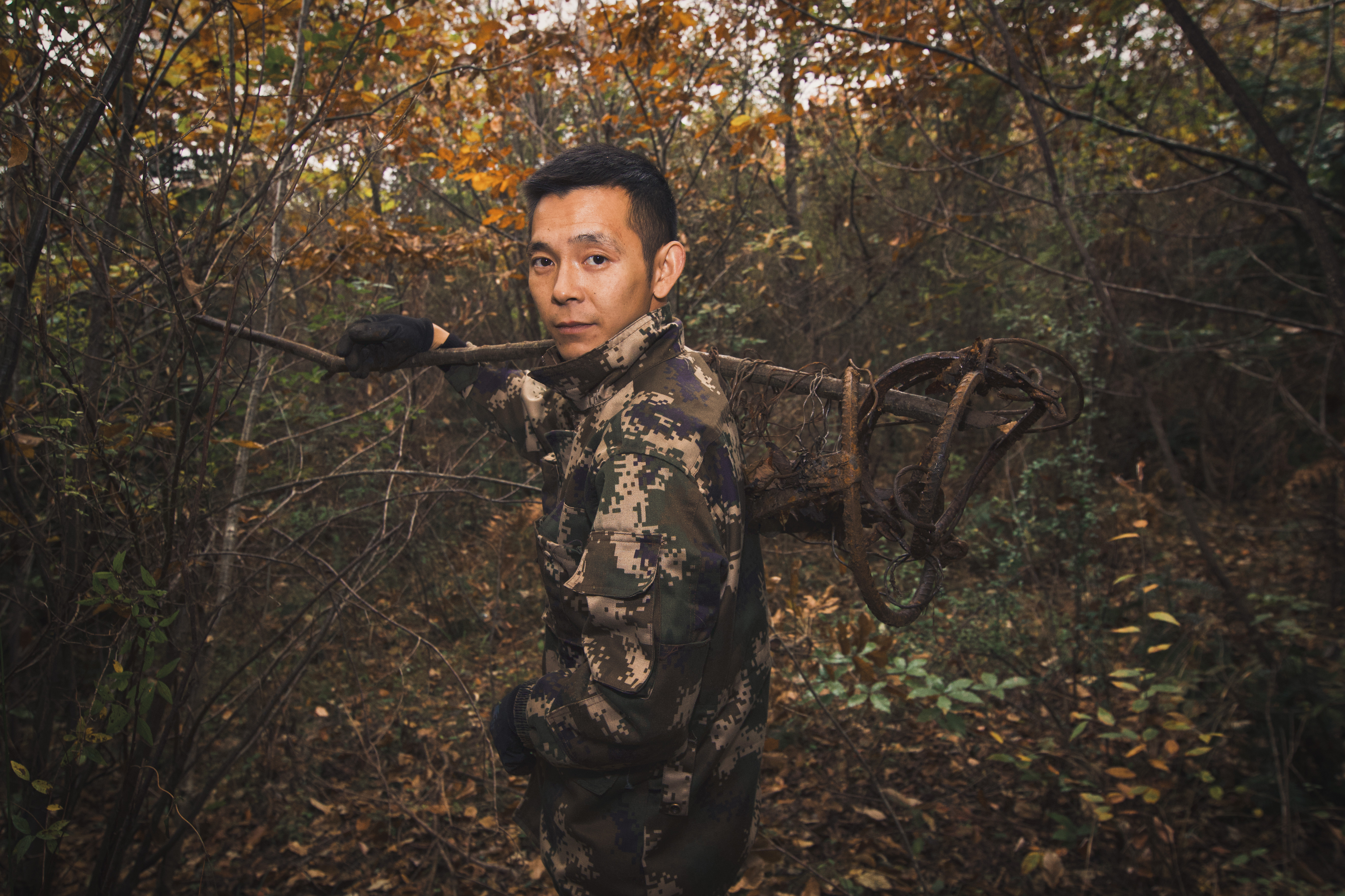 Gan Mingdong stands in a forest and holds a bear trap over his shoulder.