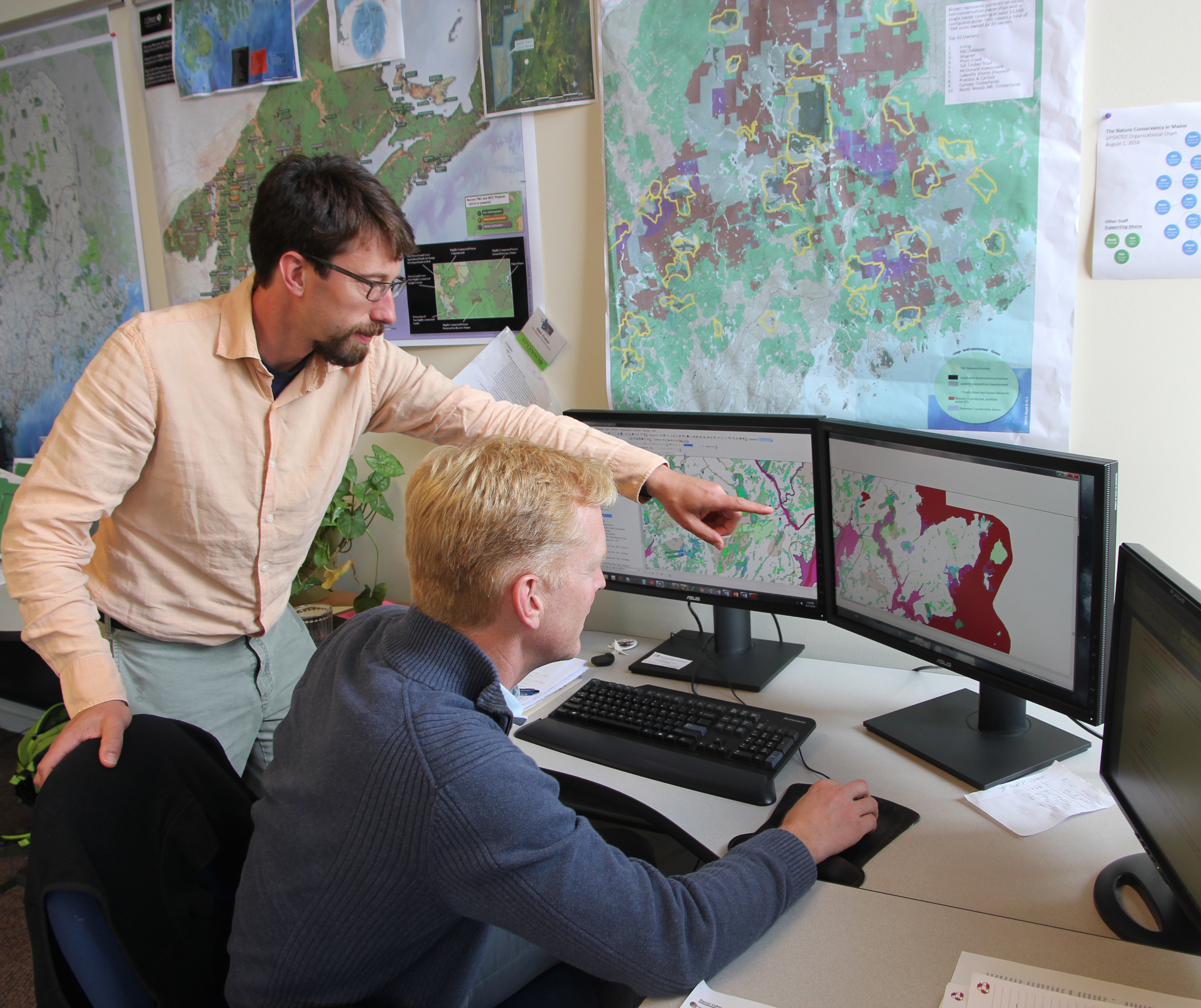 Two people work at a computer with mapping software visible.