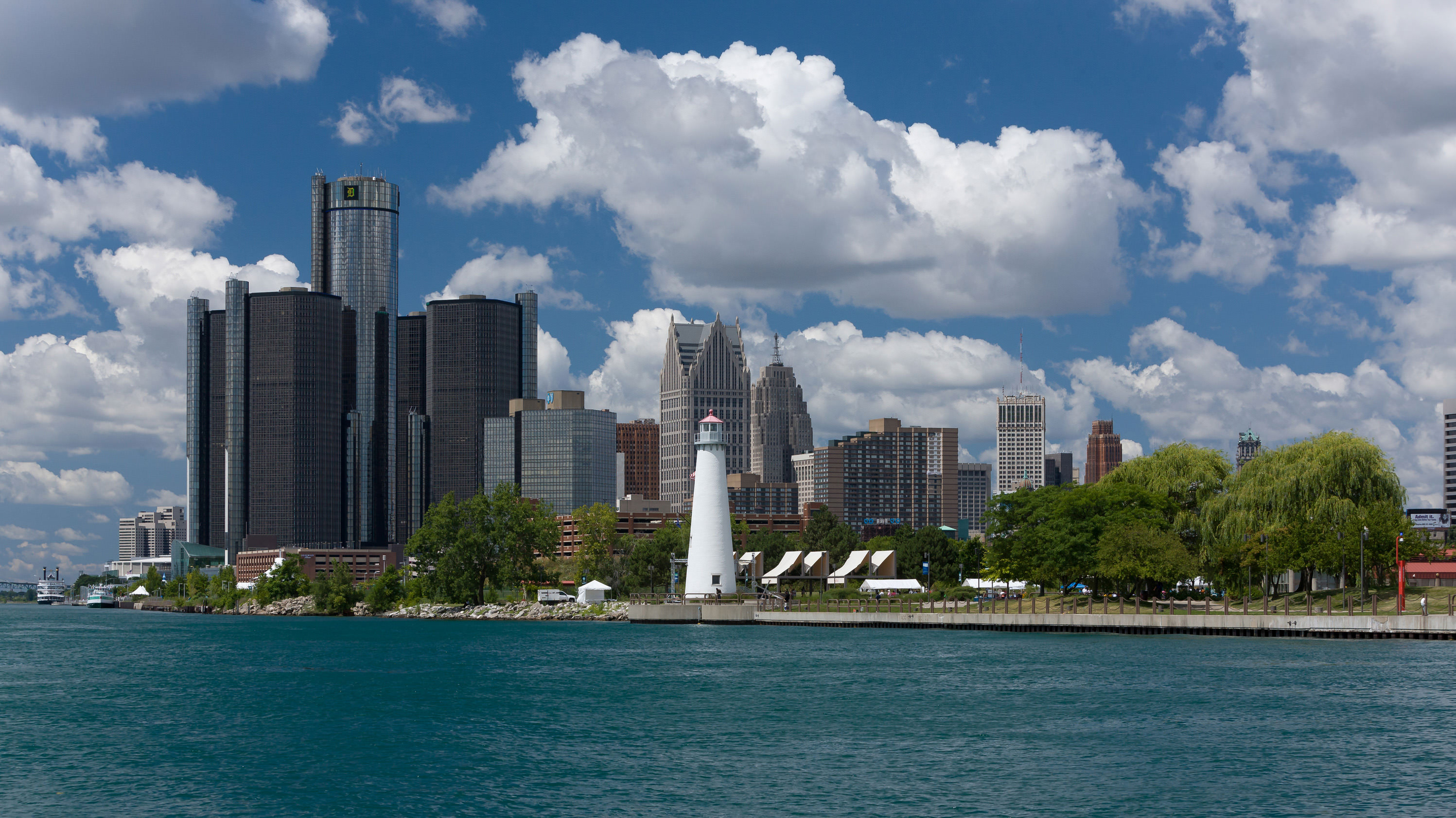 The Detroit, Michigan skyline from the water on a beautiful, sunny day. The sky is bright blue and filled with fluffy, white clouds.