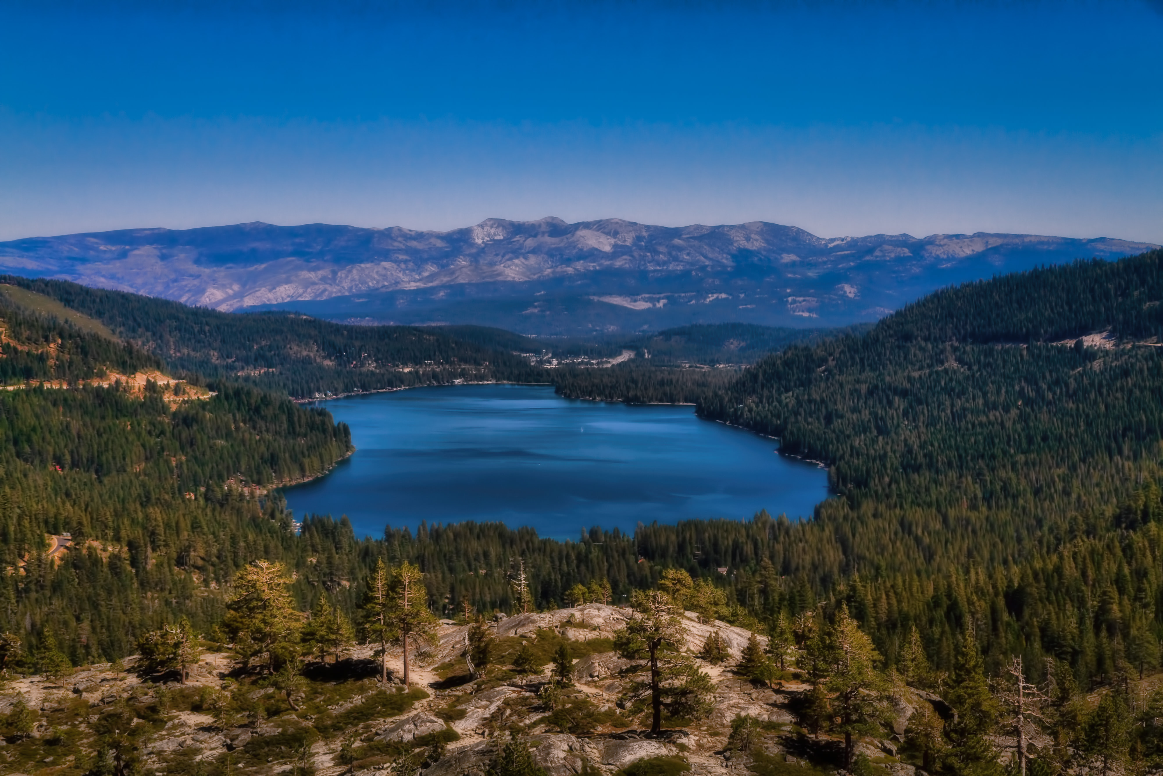 Aerial view looking down on Donner Lake, surrounded by the heavily forested ridges of the northern Sierra Mountains.