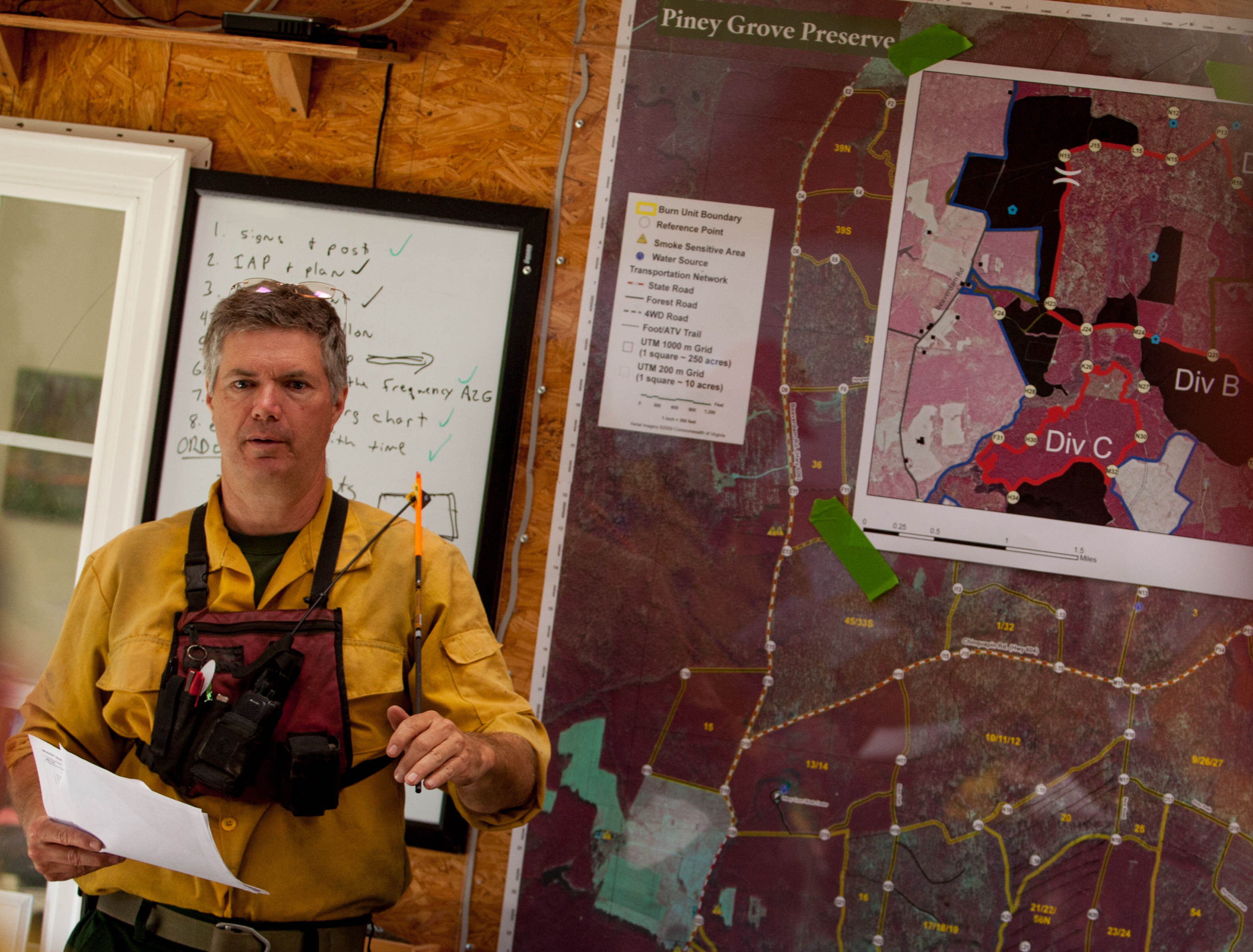 Preserve manager Bobby Clontz leads the briefing before the start of a controlled burn. A man wearing yellow fire gear stands in front of a large map showing burn areas within the preserve.