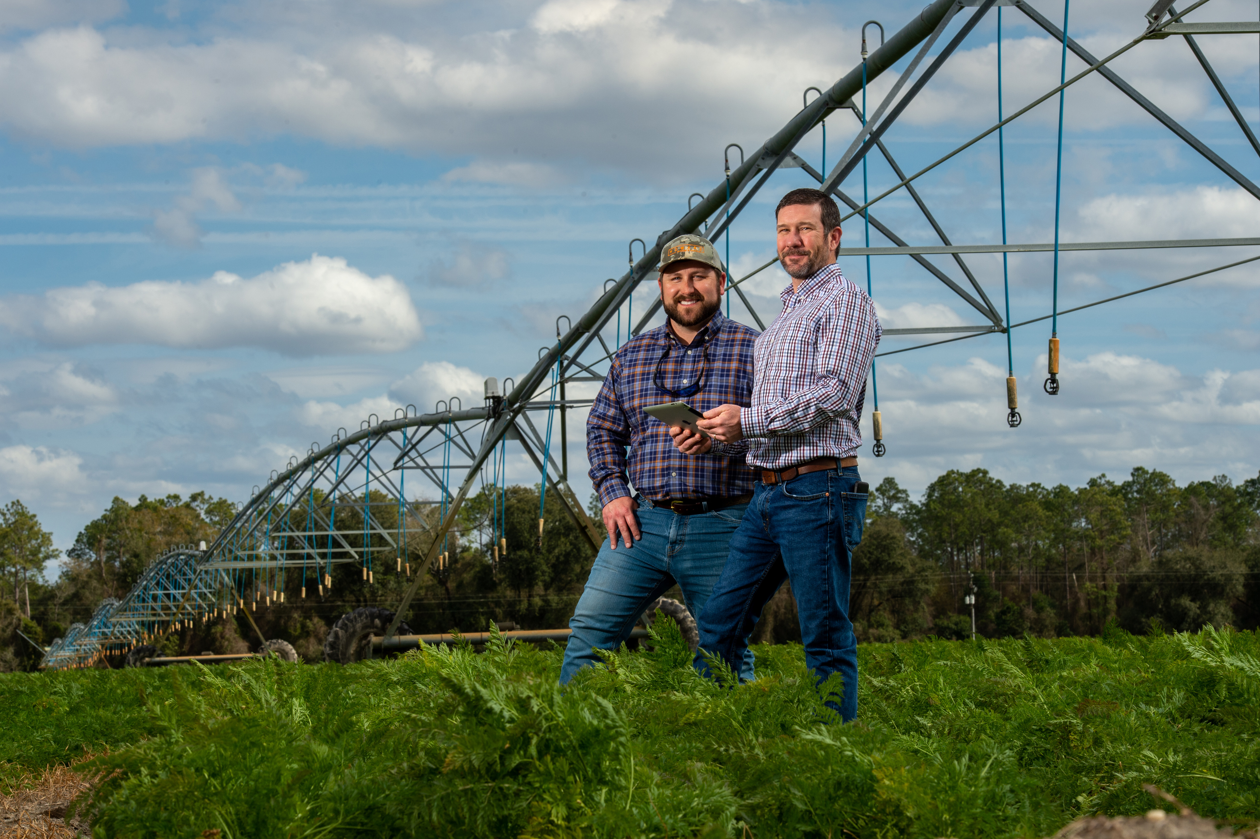Two Florida farmers in a field of greens next to an irrigation machine.