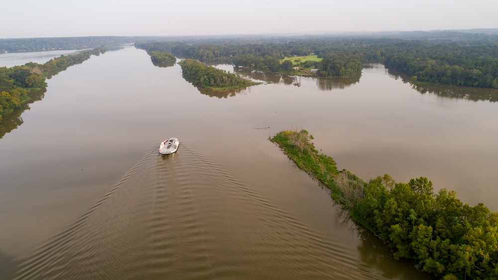 Ferry boat in the middle of a river with trees surrounding.