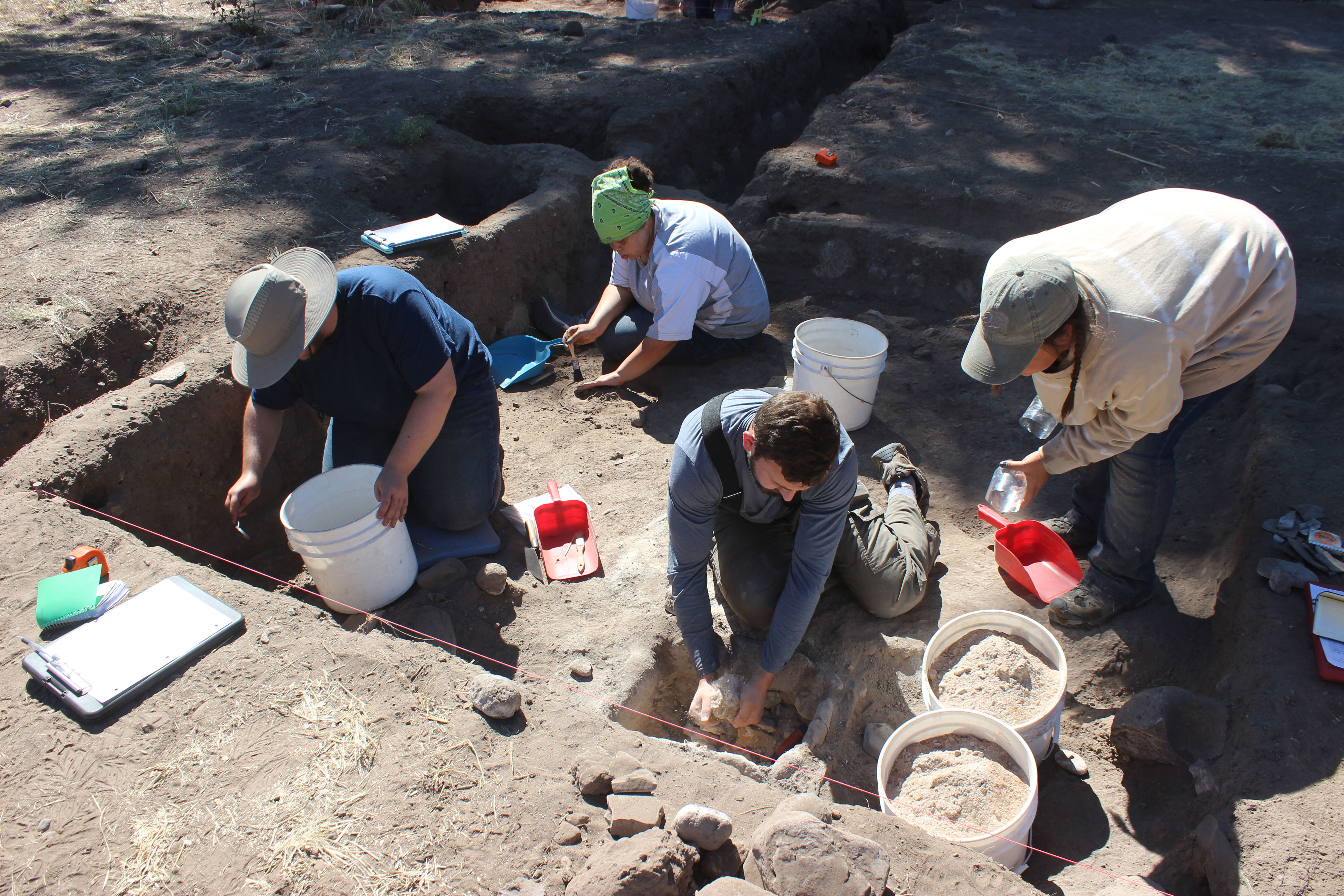 Four people with buckets excavate a site.