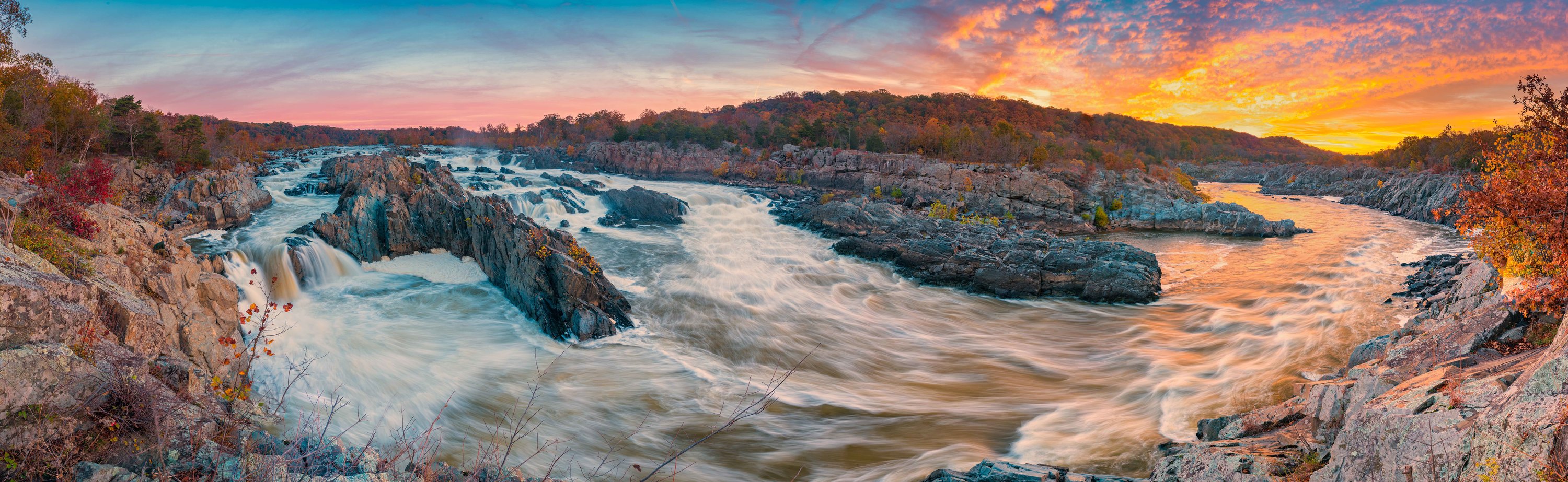 White rapids swirl and eddy as the Potomac River rushes through rocky formations at Great Falls as the sun rises.