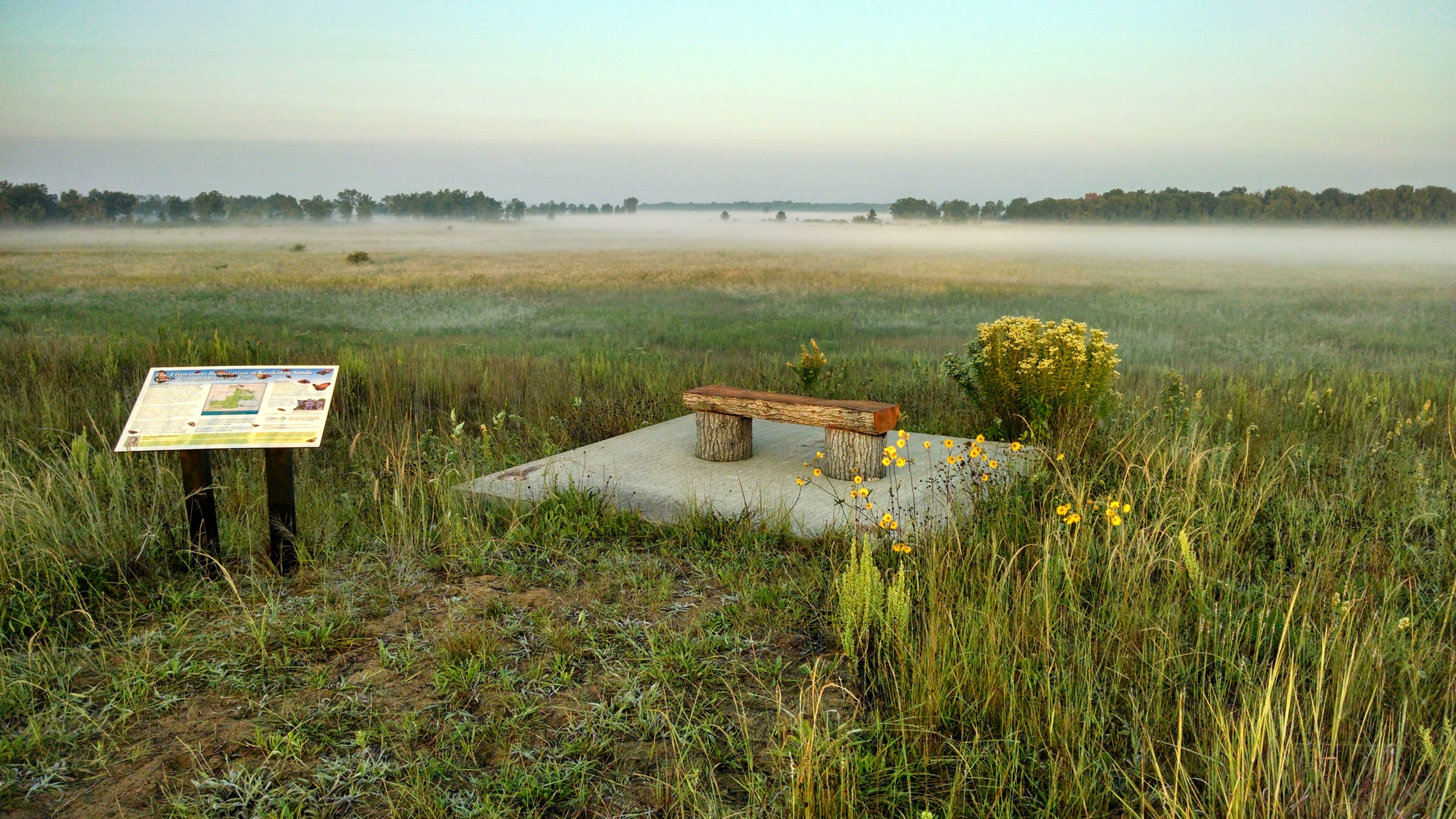 An overlook with signage and a bench looking out onto a misty prairie landscape.