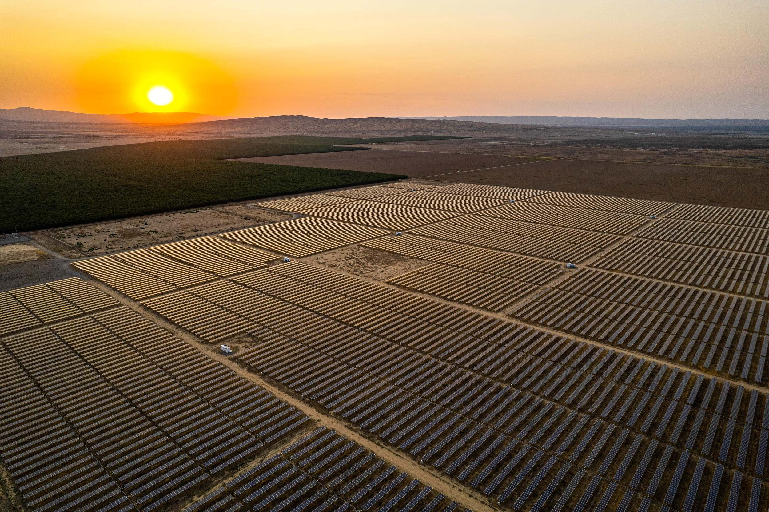 An aerial image of a field covered in solar panels and a sunset.