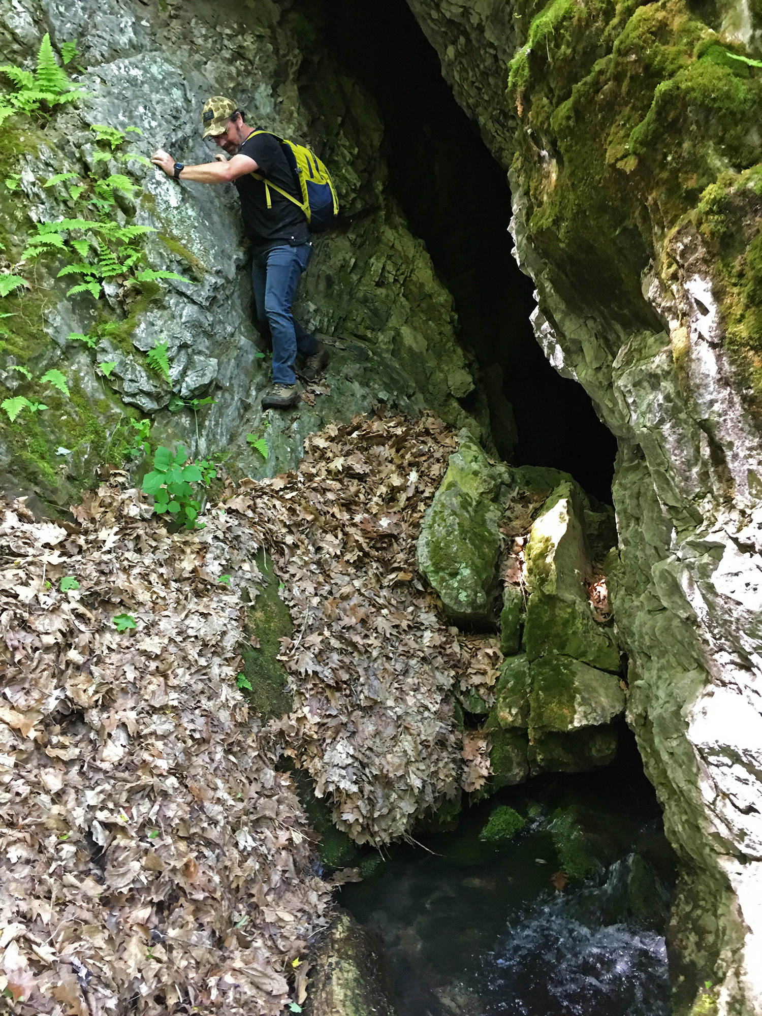 A man balances on a narrow rock ledge as he carefully inches his way out of a mountain cave.