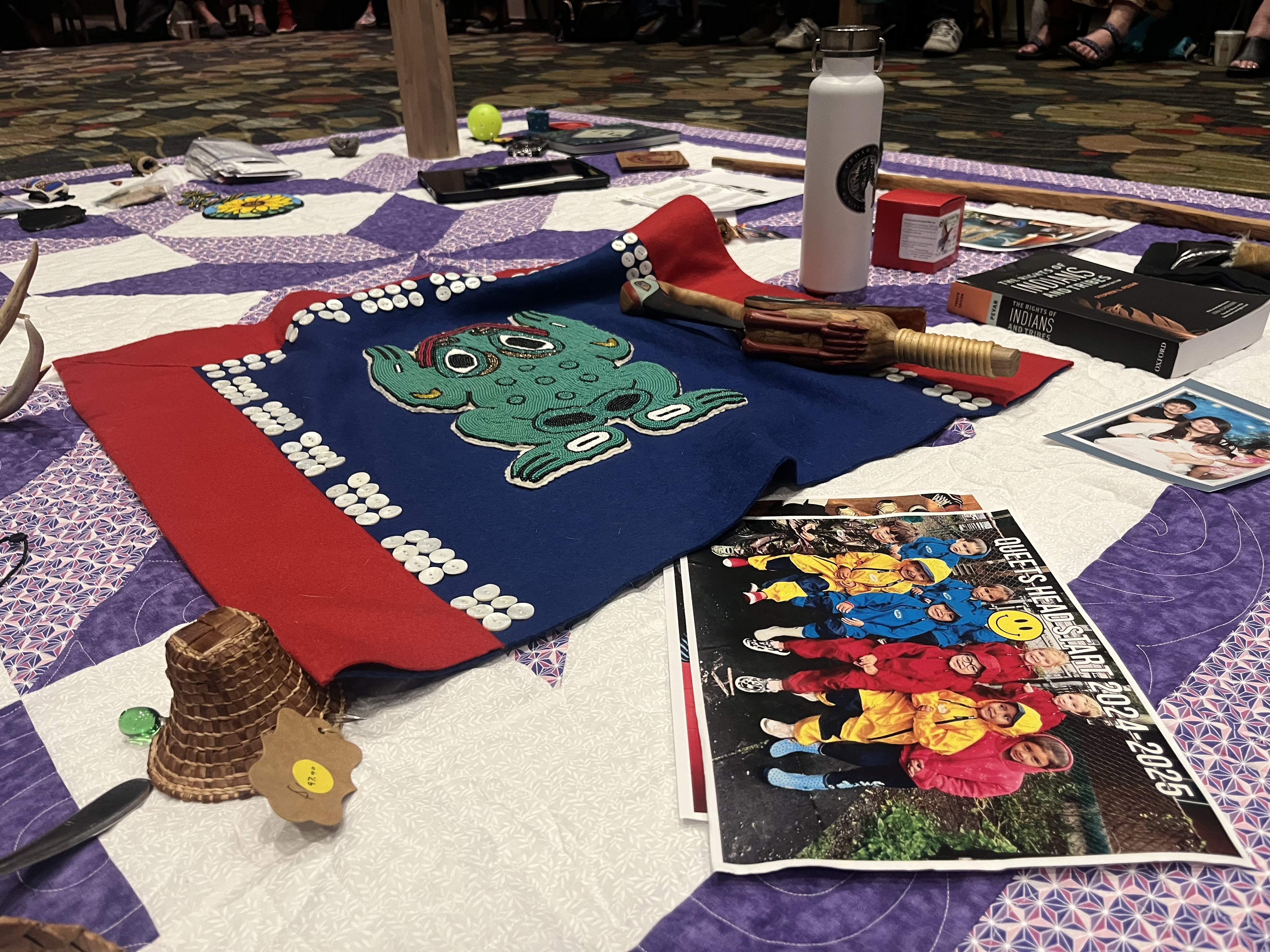 Water bottle, banner, weaving and other items laying on a purple quilt gifted by the Haudenosaunee Confederacy.