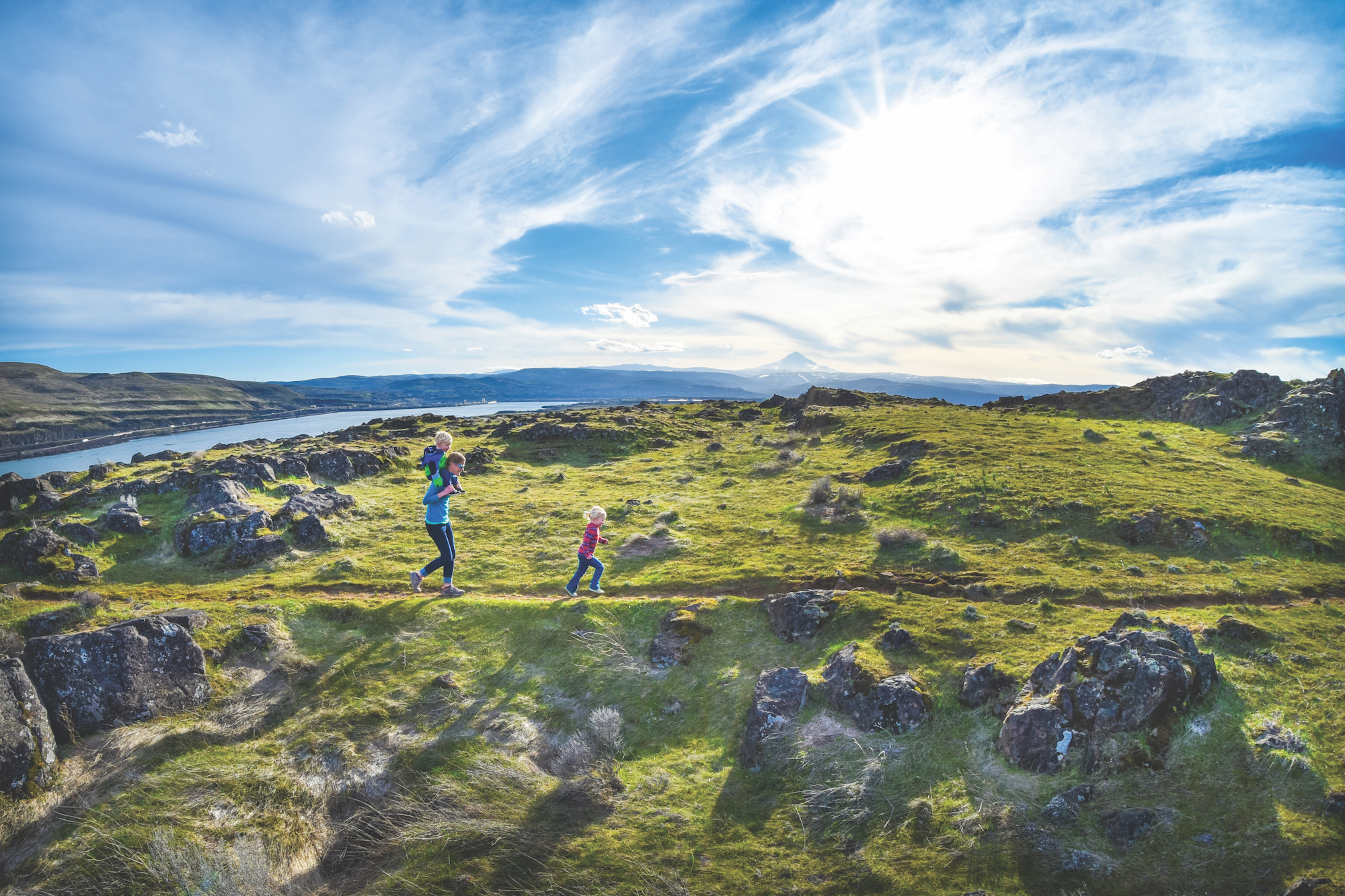 A family runs on a hiking path with a scenic Oregon vista in the background with a river and Mount Hood in the background.