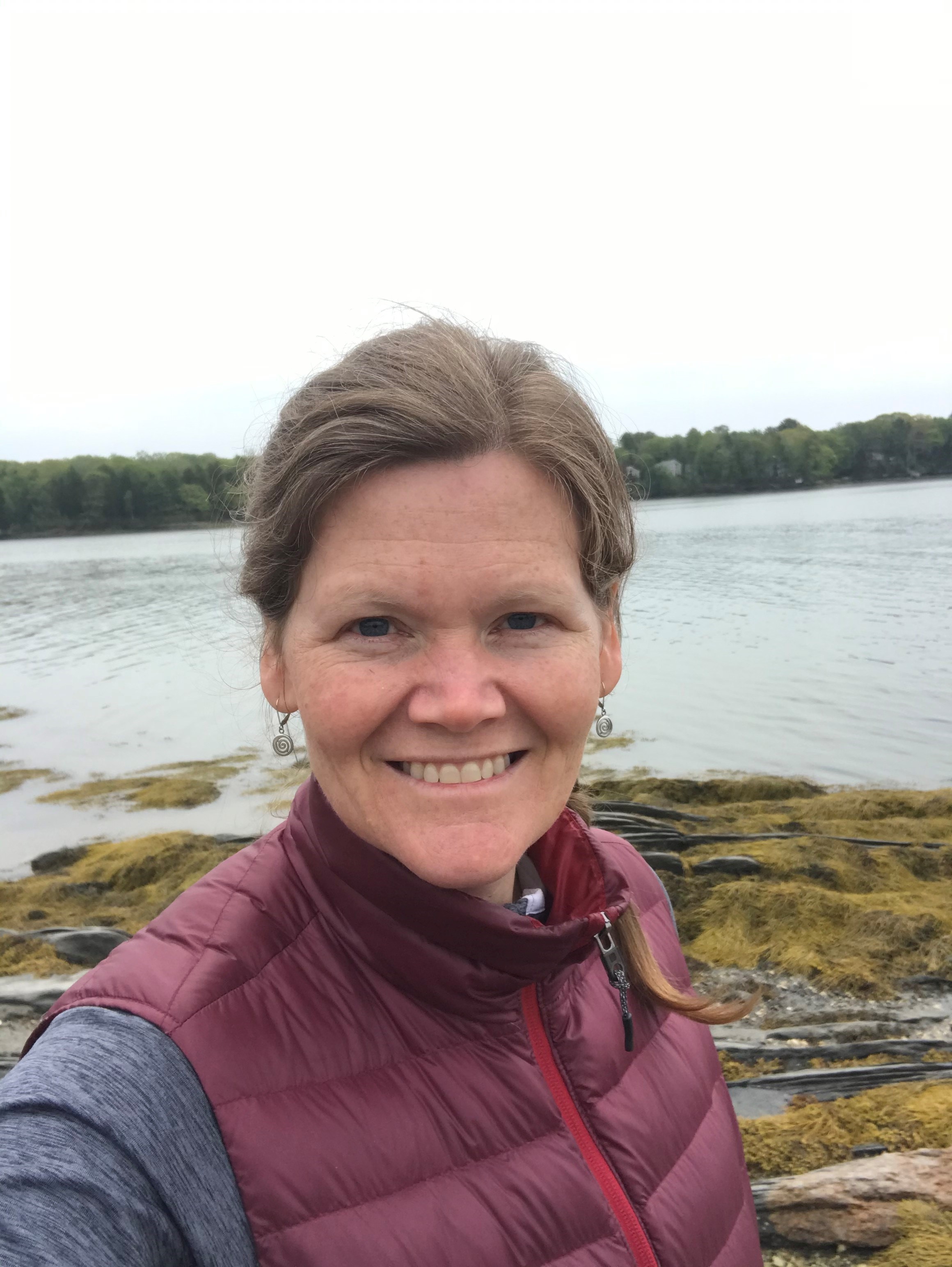 A selfie of Jessica Rice-Healey in front of a rocky shoreline.