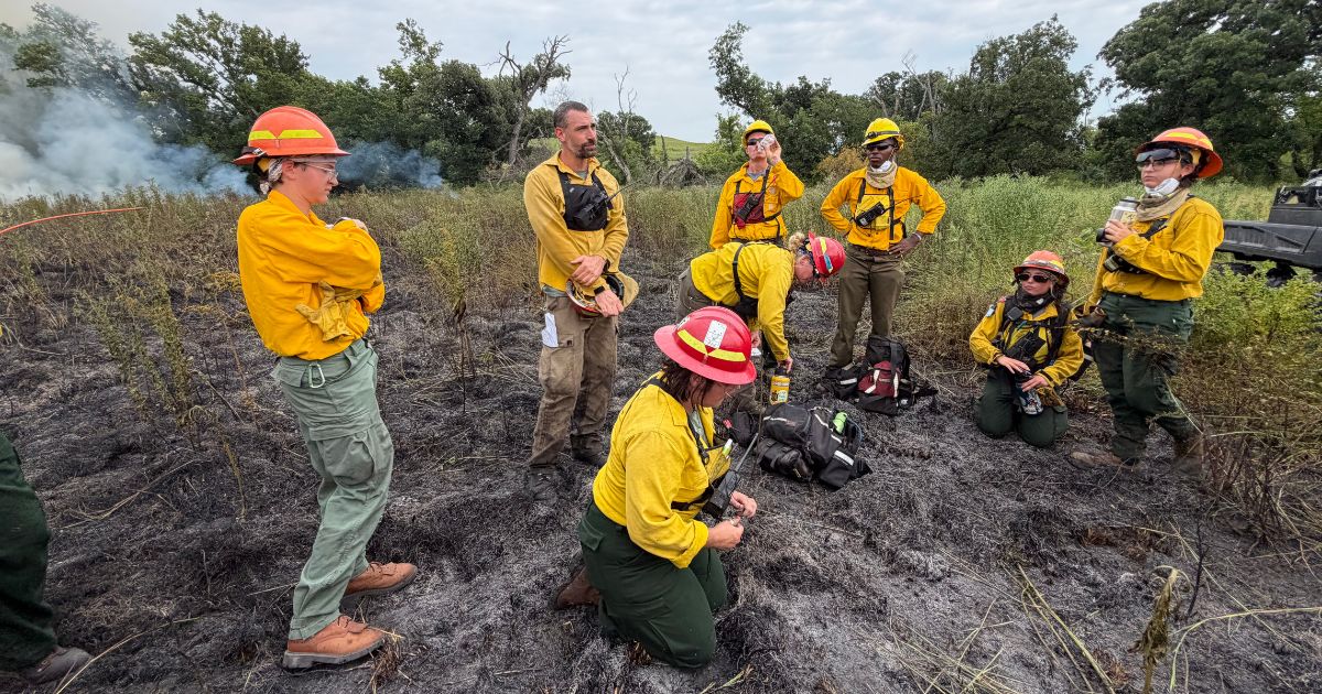 A group of TNC employees huddle together in their bright yellow fire gear during their prescribed burn training. 