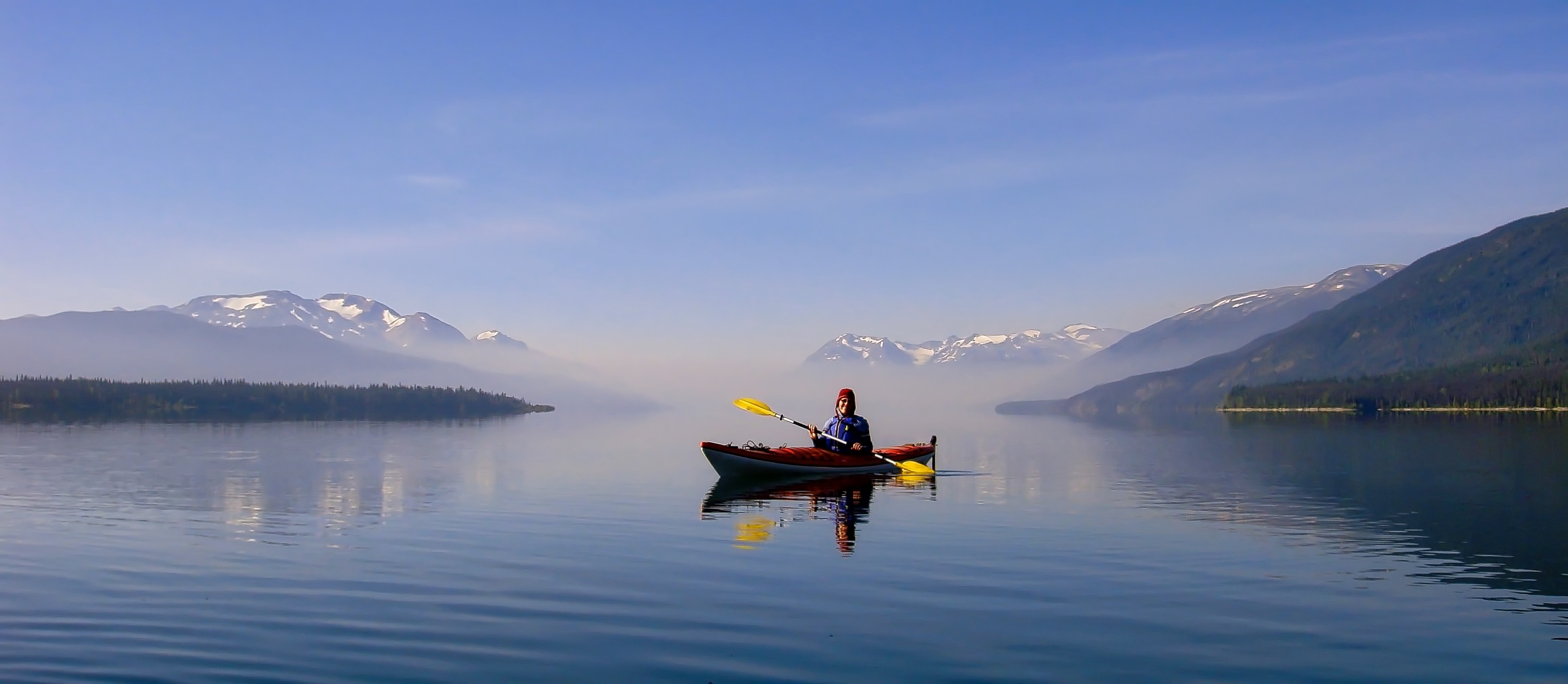 A person in a kayak at Morice Lake, British Columbia, Canada, with distant smoke from a forest fire.