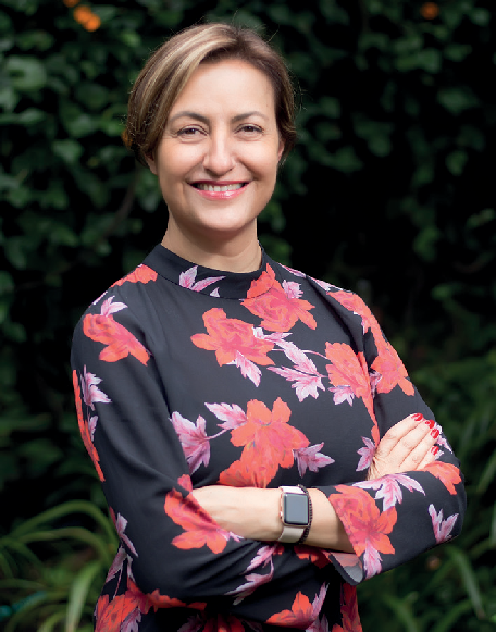 A woman with a floral blouse stands smiling at the camera. 