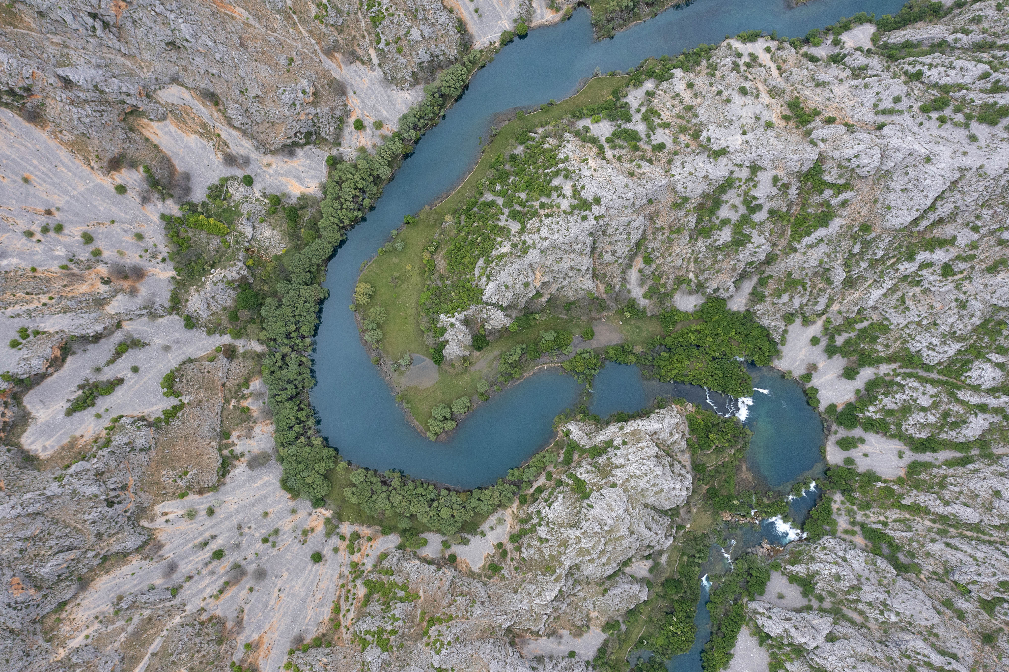 Aerial view looking straight down on a river that winds in an S curve through rocky terrain.